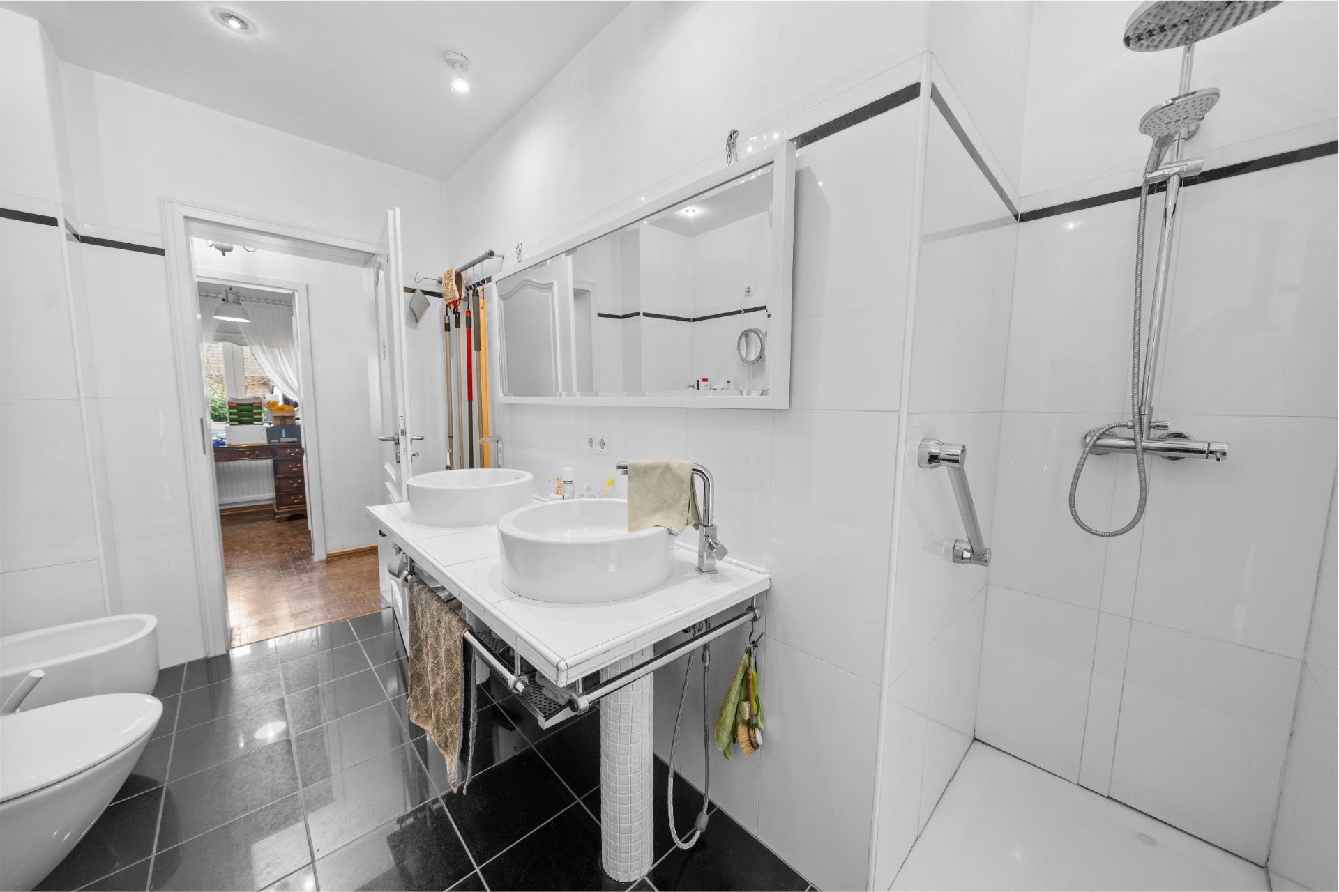 Modernes Badezimmer mit zwei Waschbecken, großer Dusche, Bidet und schwarzem Fliesenboden.