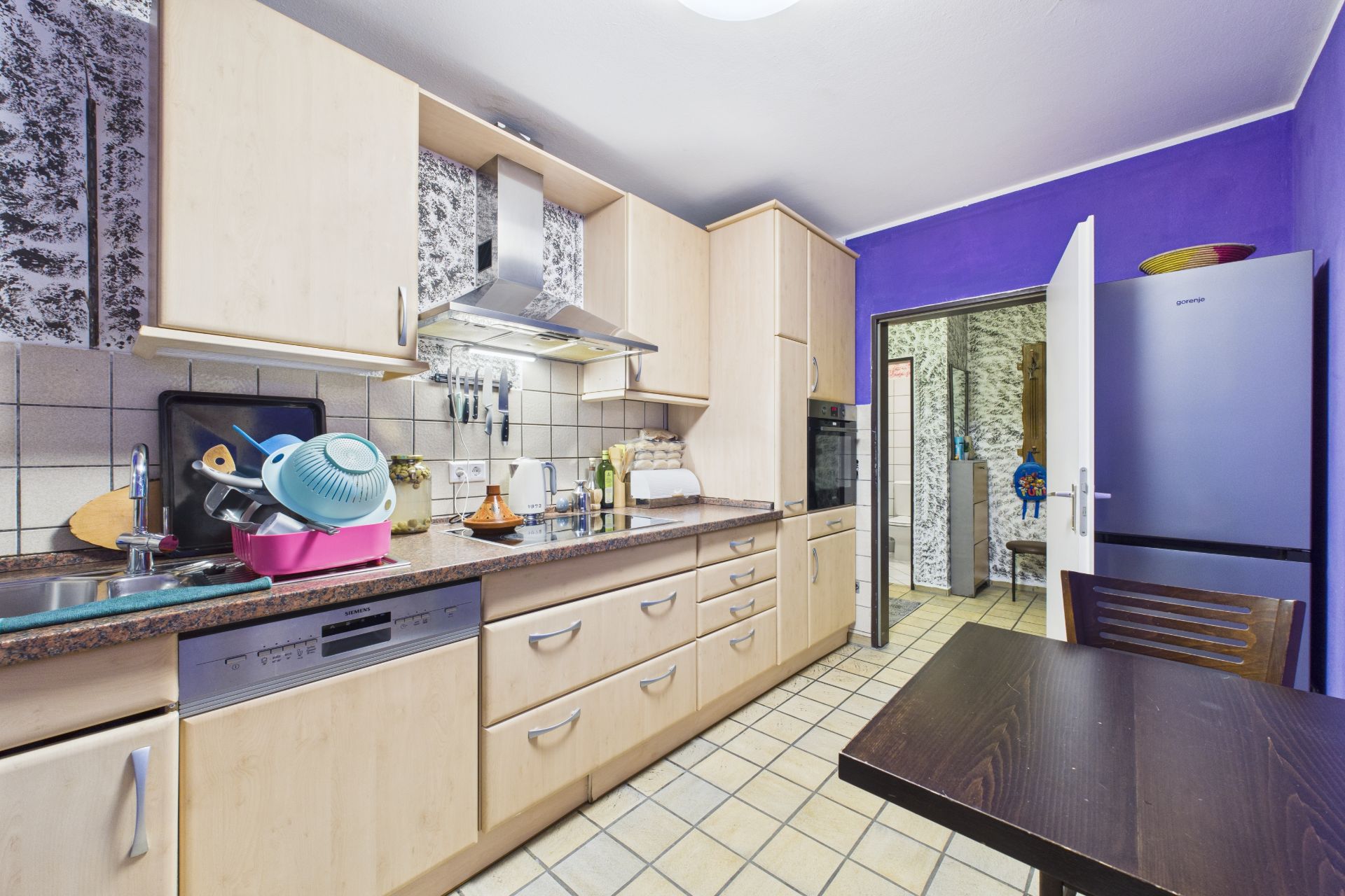Moderne Küche mit Holzmöbeln, Spülmaschine, offenem Kühlschrank und Esstisch, Wand in Lila gestrichen.