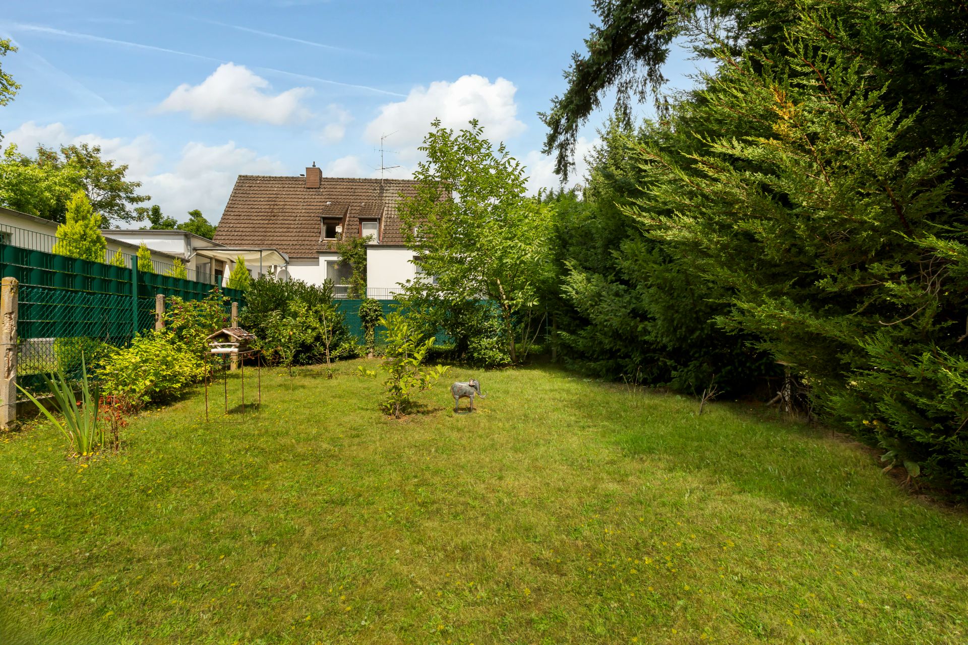 Grüner Garten mit Rasen, Bäumen und Büschen, umzäunt und bei Tageslicht fotografiert.