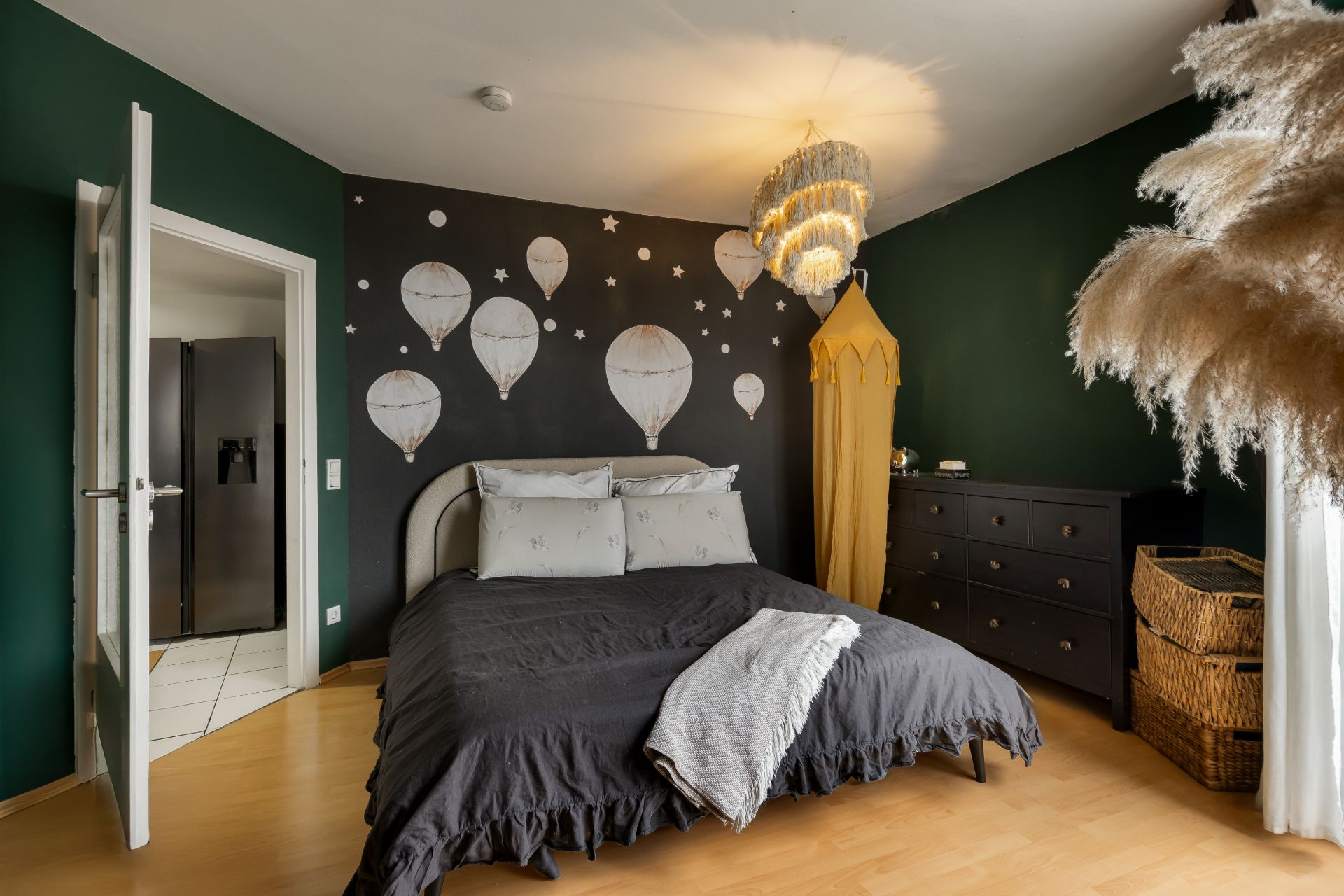 Schlafzimmer mit grün-schwarzen Wänden, Doppelbett, Ballonwanddeko und Kommode.