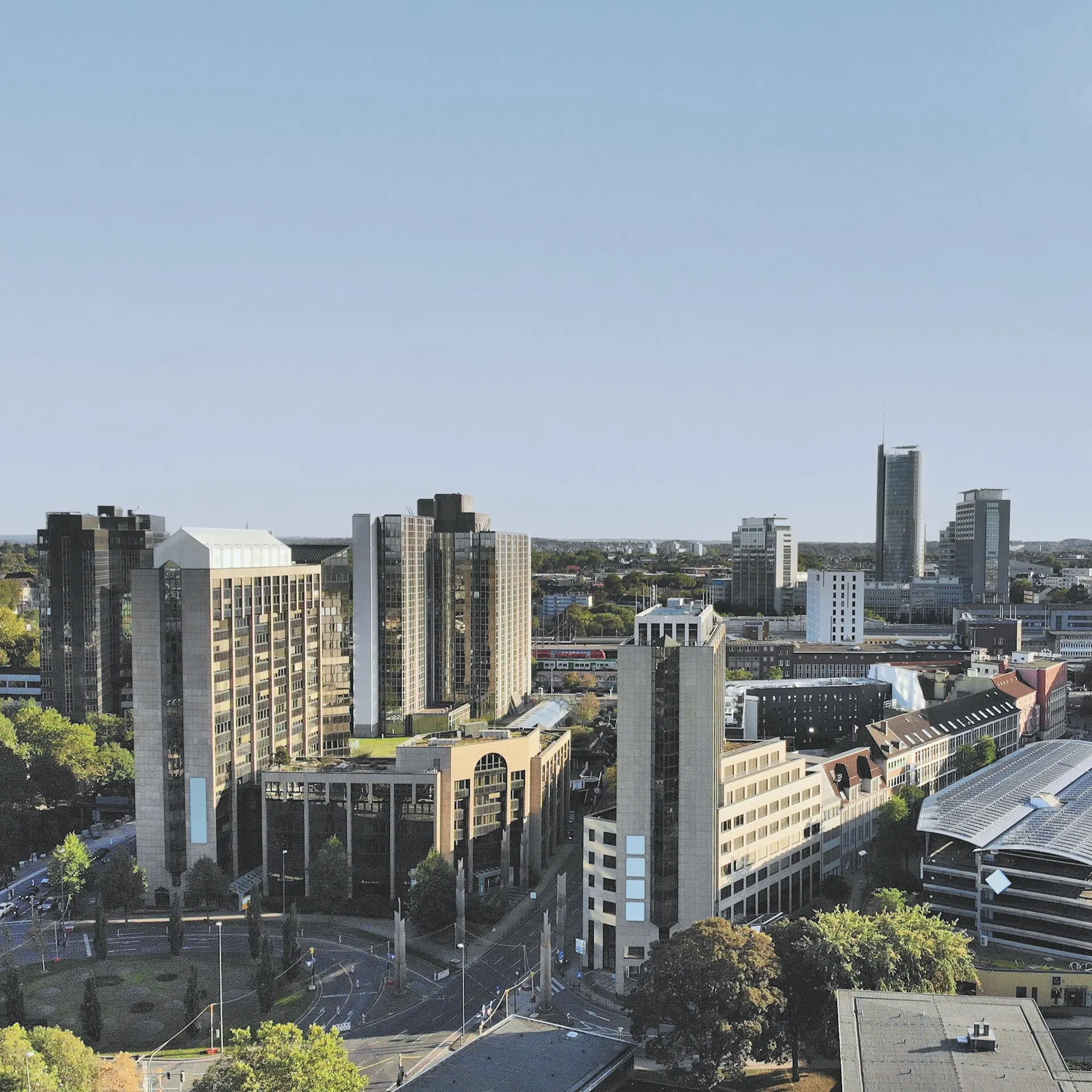 Stadtansicht mit mehreren modernen Hochhäusern und Bäumen im Vordergrund.