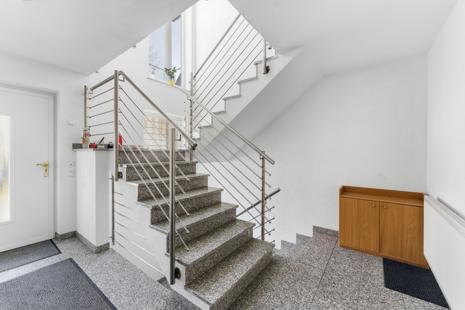 Treppenhaus mit Granitstufen, Metallgeländer und einem Holzschrank an der Wand.
