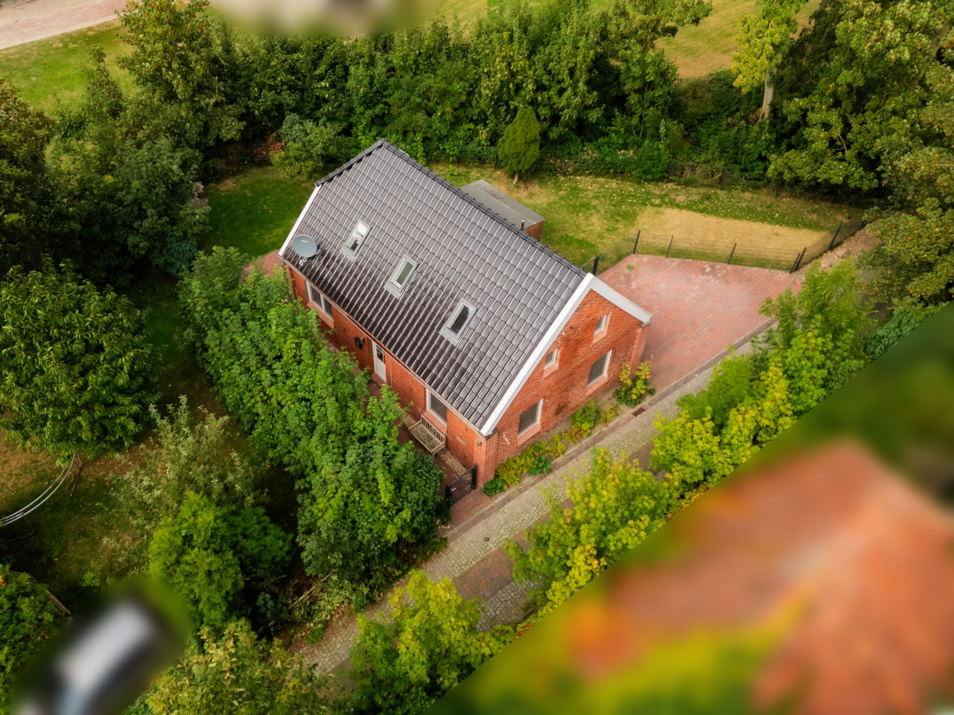 Luftaufnahme eines roten Einfamilienhauses mit grauem Dach und umliegendem Garten.