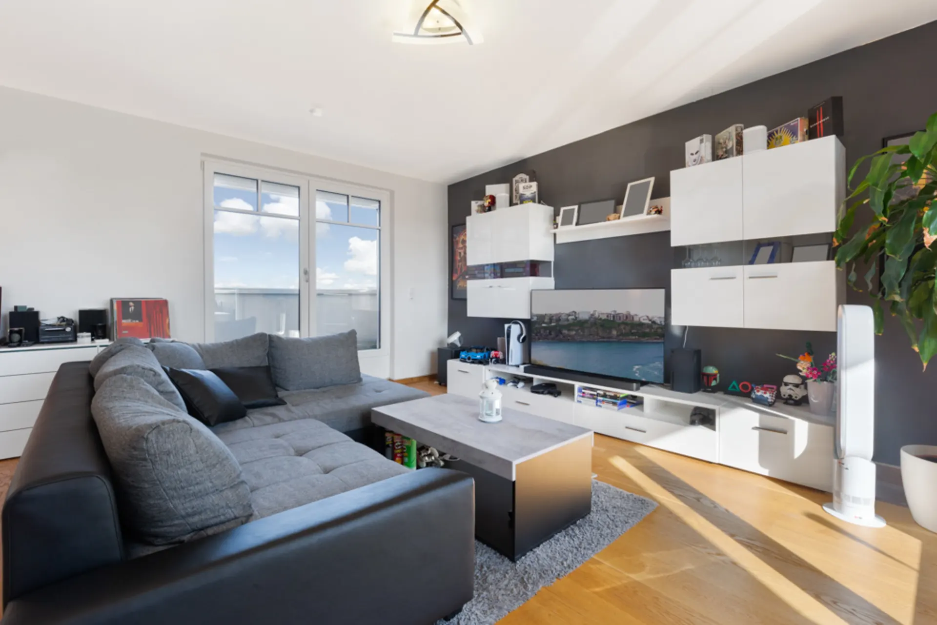 Modernes Wohnzimmer mit grauem Sofa, Couchtisch, Fernseher und weißen Wandregalen.