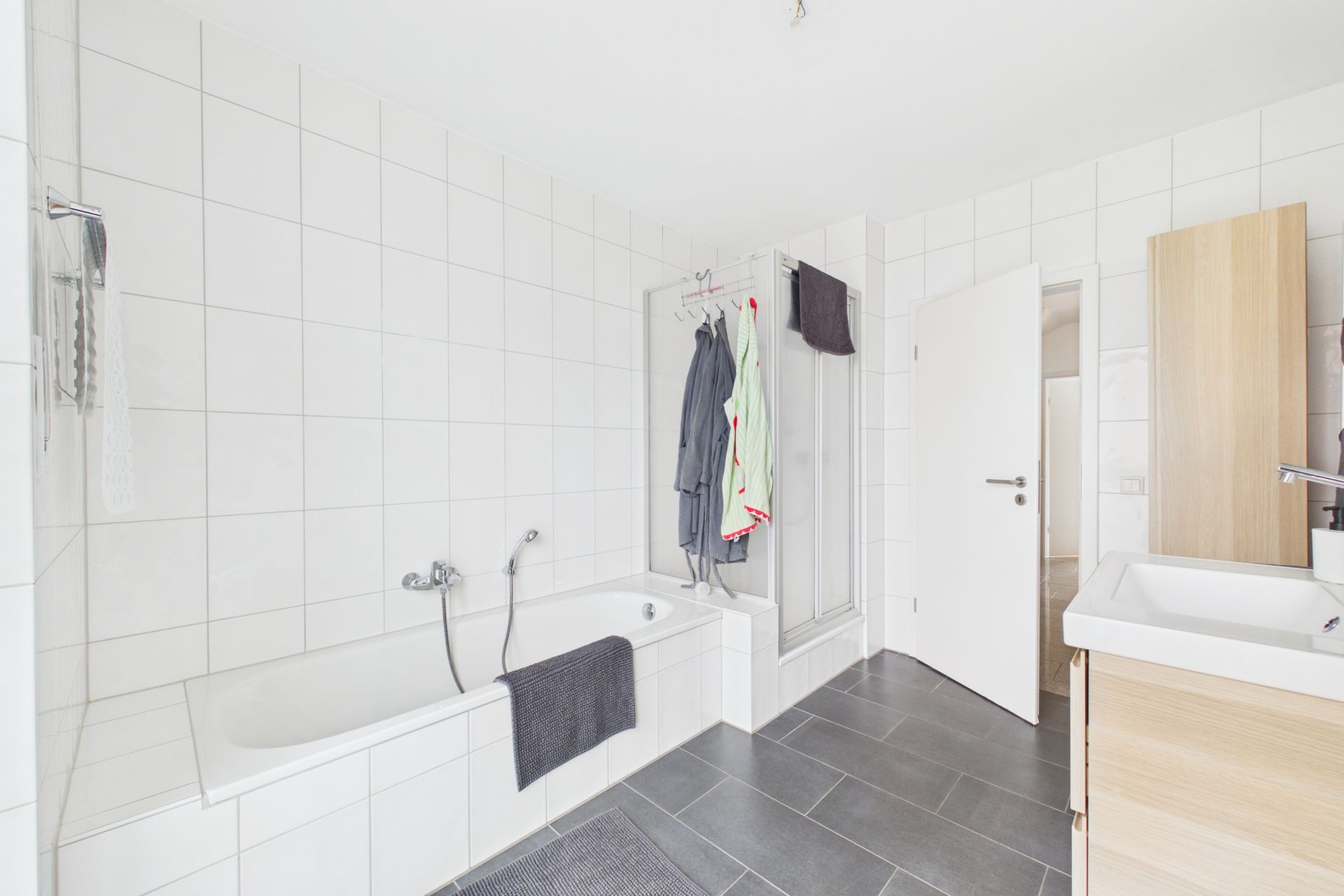 Modernes Badezimmer mit Badewanne, Dusche, Waschbecken und Handtüchern an der Wand.