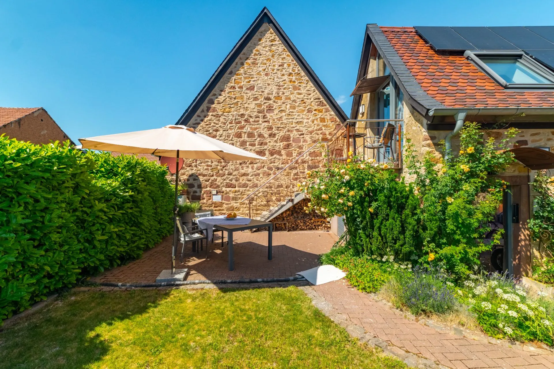 Gepflegter Garten mit Sitzbereich, Sonnenschirm und Steinhaus im Hintergrund.