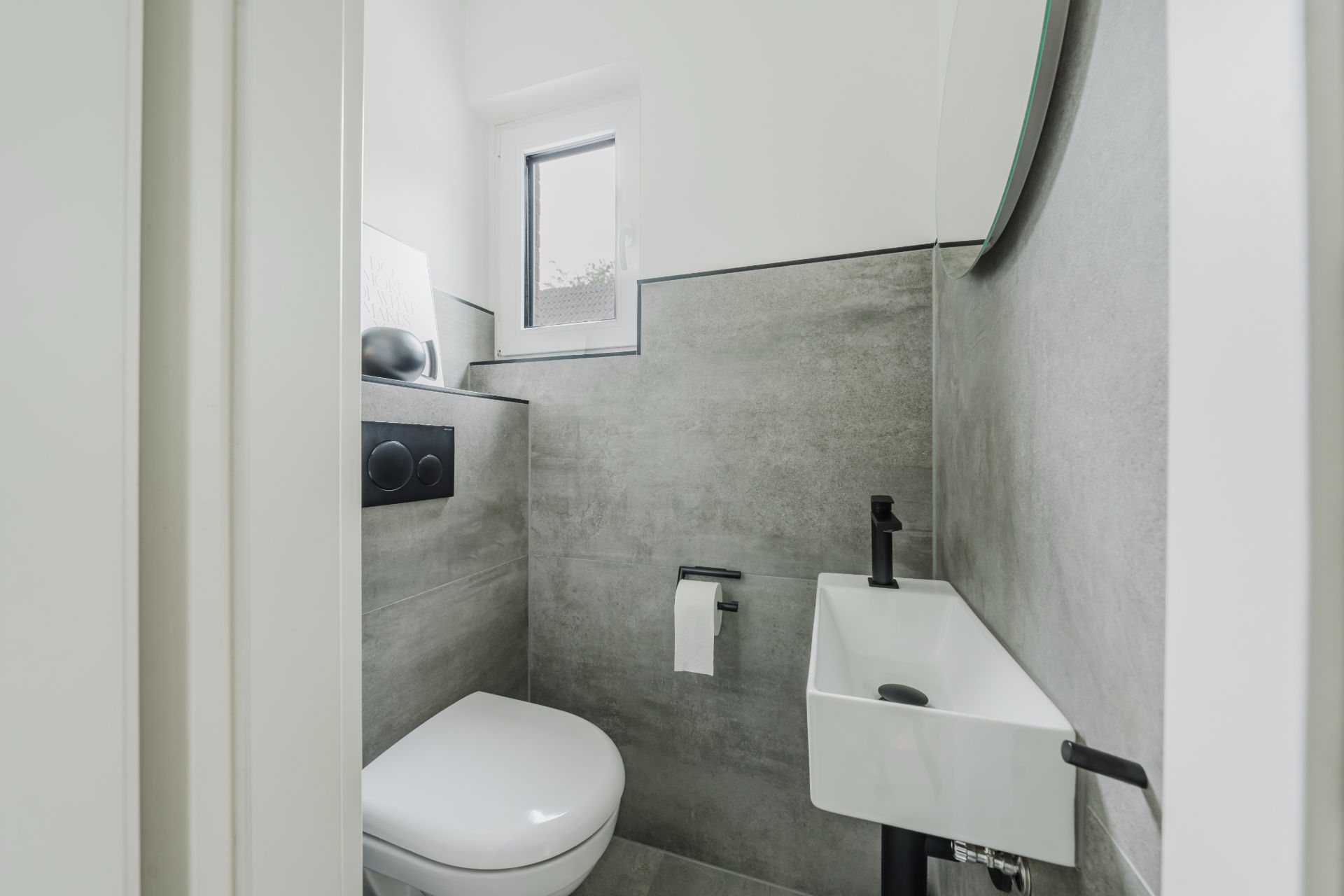 Modernes, kleines Badezimmer mit WC, kleinem Waschbecken und Fenster.