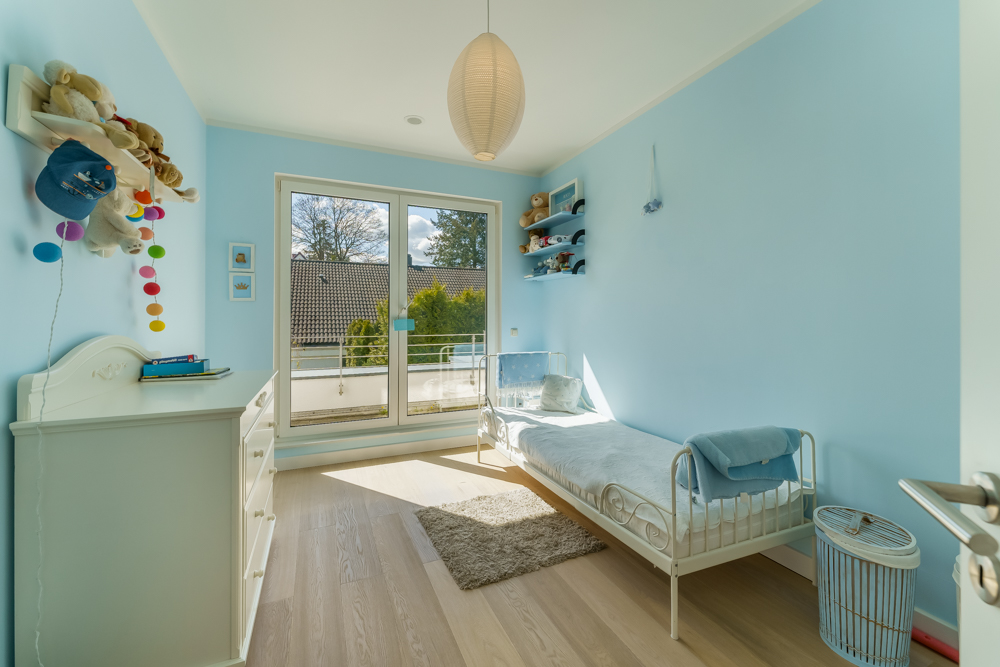 Helles Kinderzimmer mit blau gestrichenen Wänden, Einzelbett, Kommode und großem Fenster.