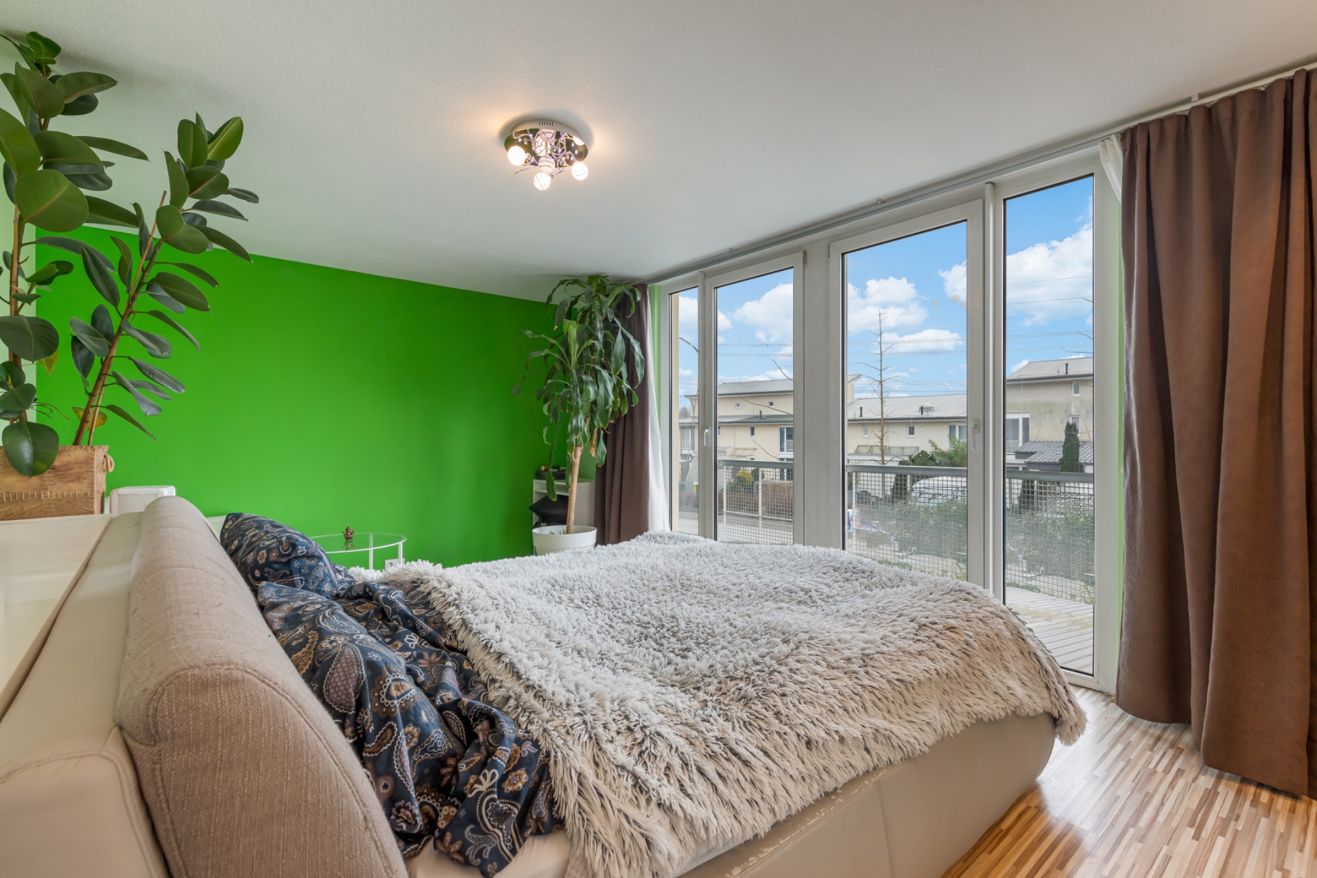 Helles Schlafzimmer mit grün gestrichener Wand, großem Fenster und Pflanzen.