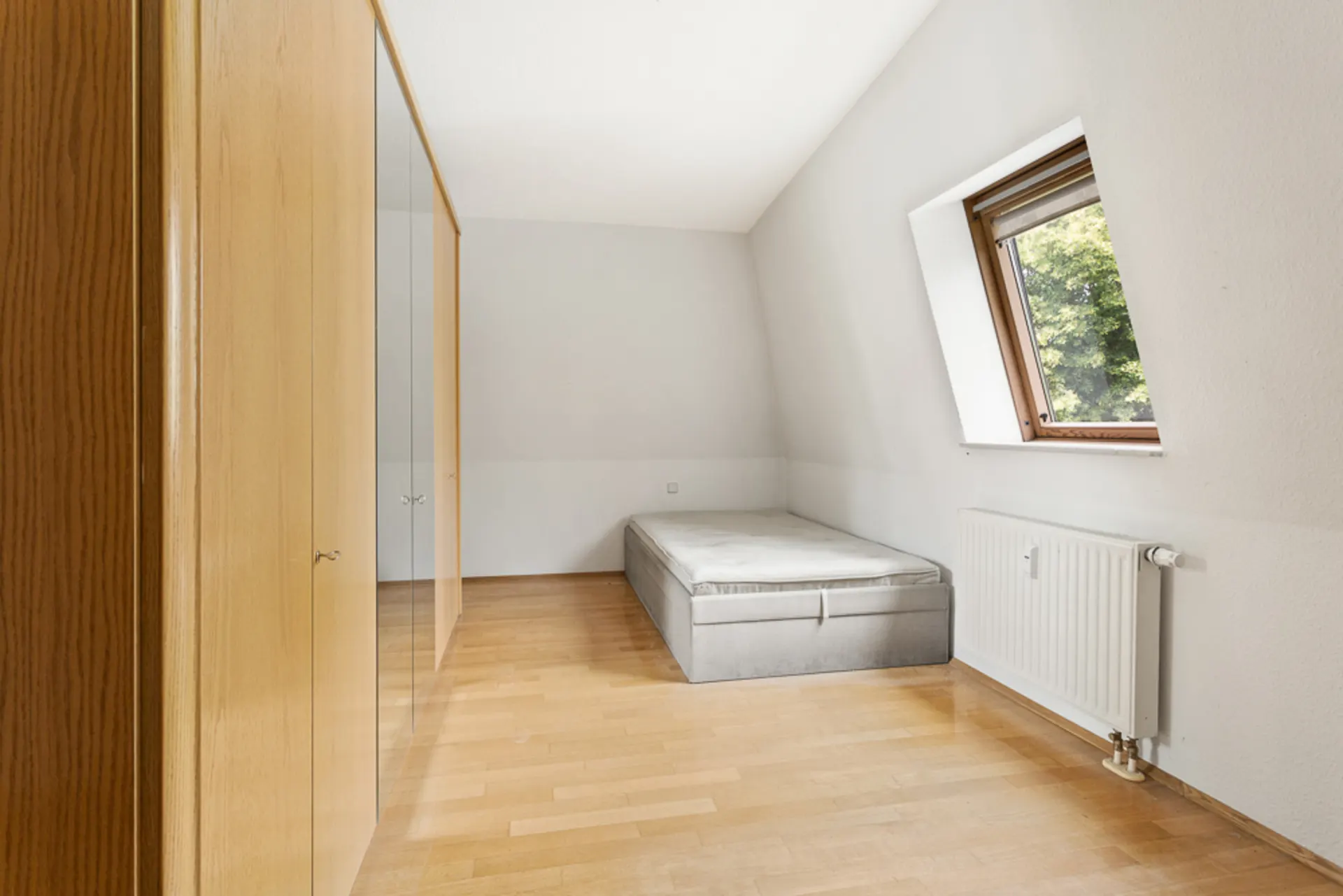 Helles Schlafzimmer mit großem Schrank, Einzelbett und Fenster mit Ausblick ins Grüne.