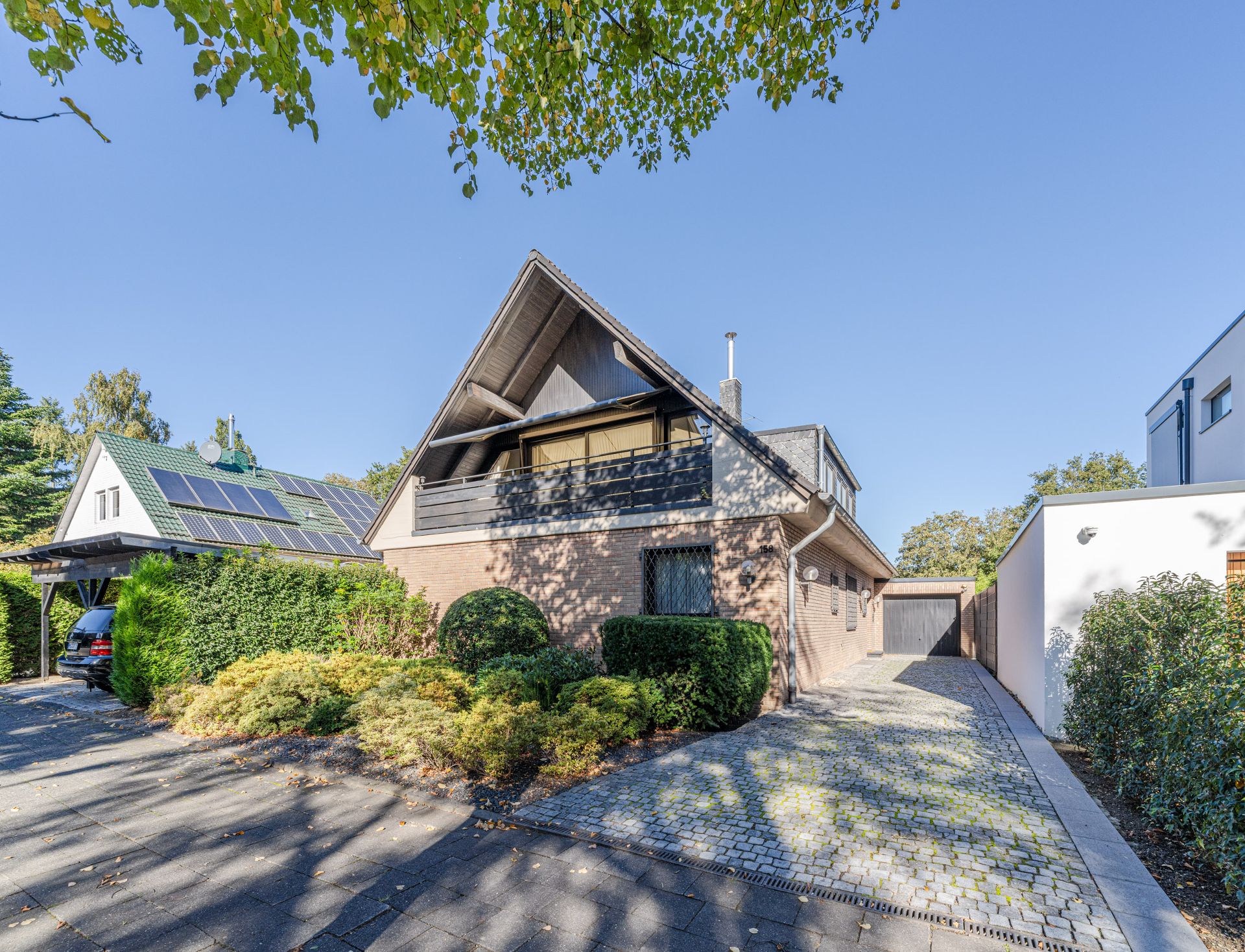Haus mit spitzem Dach, großer Auffahrt und gepflegtem Vorgarten an einem sonnigen Tag.