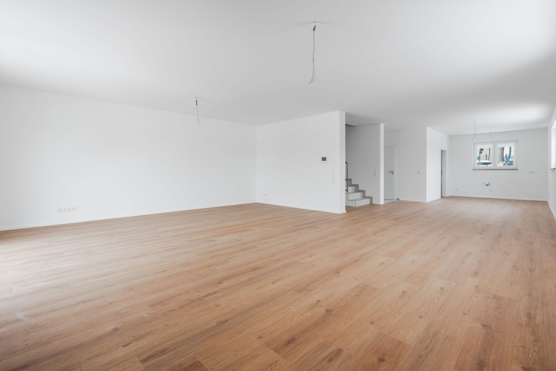 Leerer Raum mit Holzfußboden, weißen Wänden und Treppe, Fenster im Hintergrund.