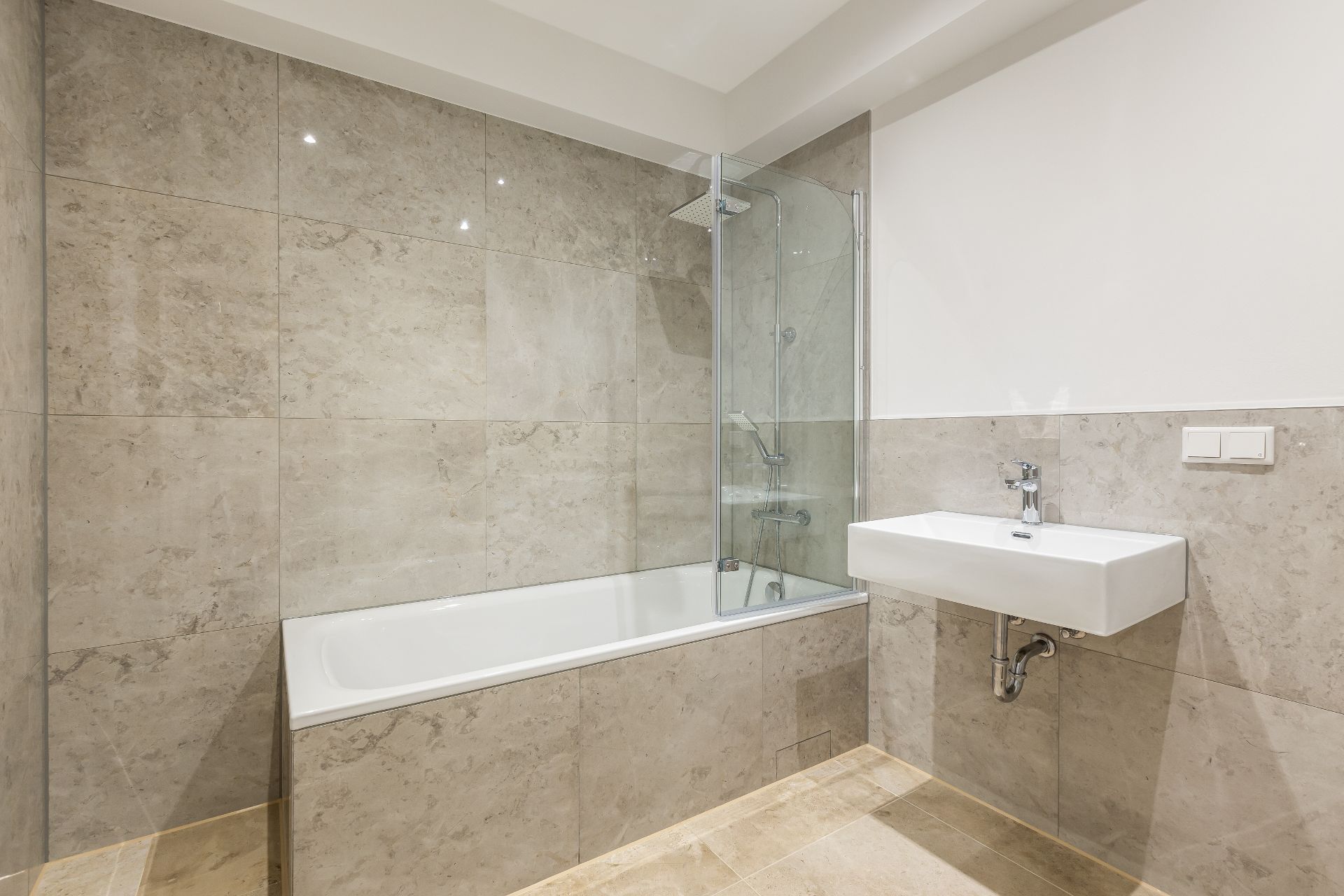 Modernes Bad mit Badewanne, Glasduschwand und rechteckigem Waschbecken an gefliester Wand.