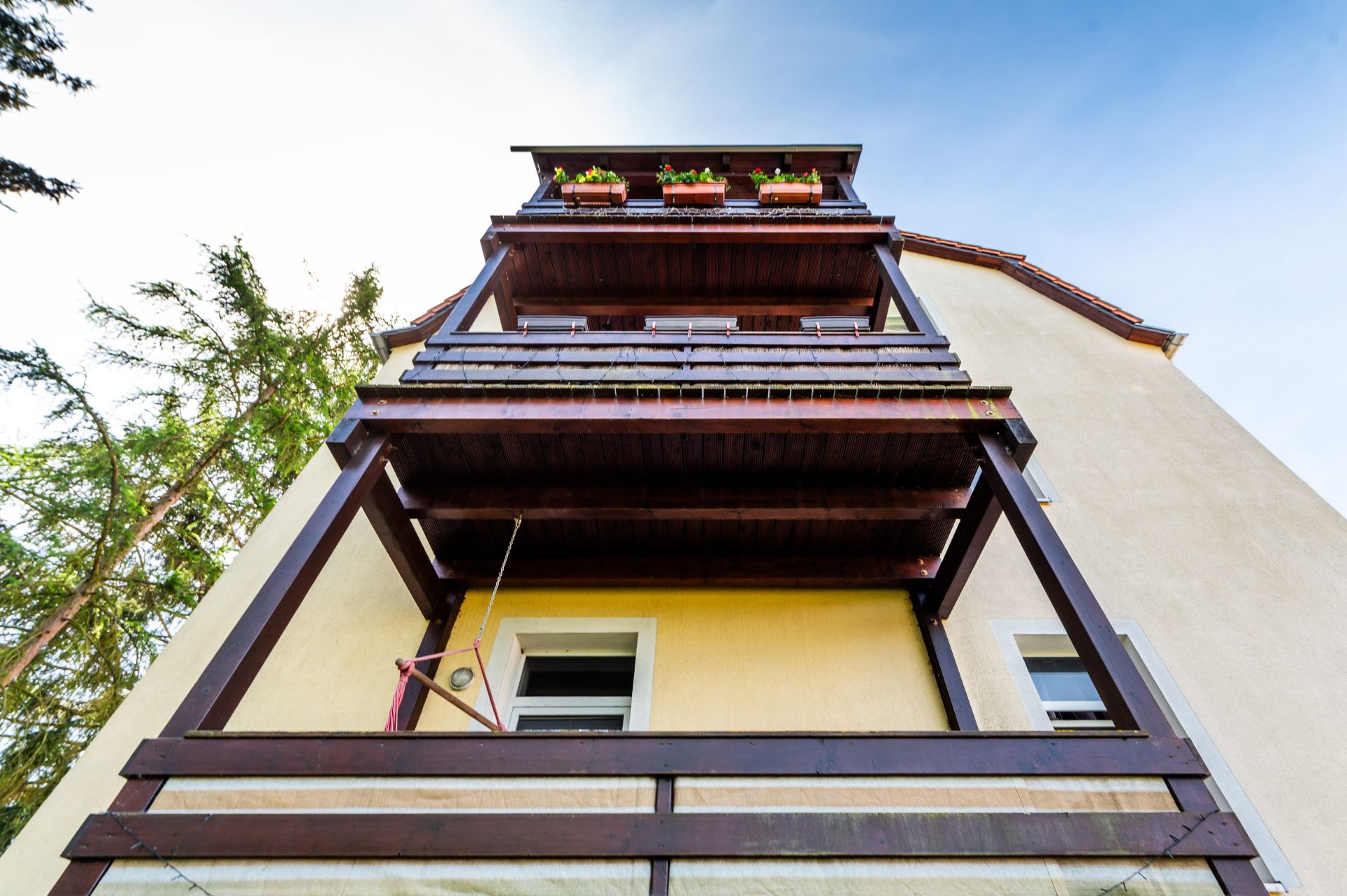 Blick nach oben auf ein mehrstöckiges Wohnhaus mit mehreren Holz-Balkonen und Blumen auf dem obersten Balkon.