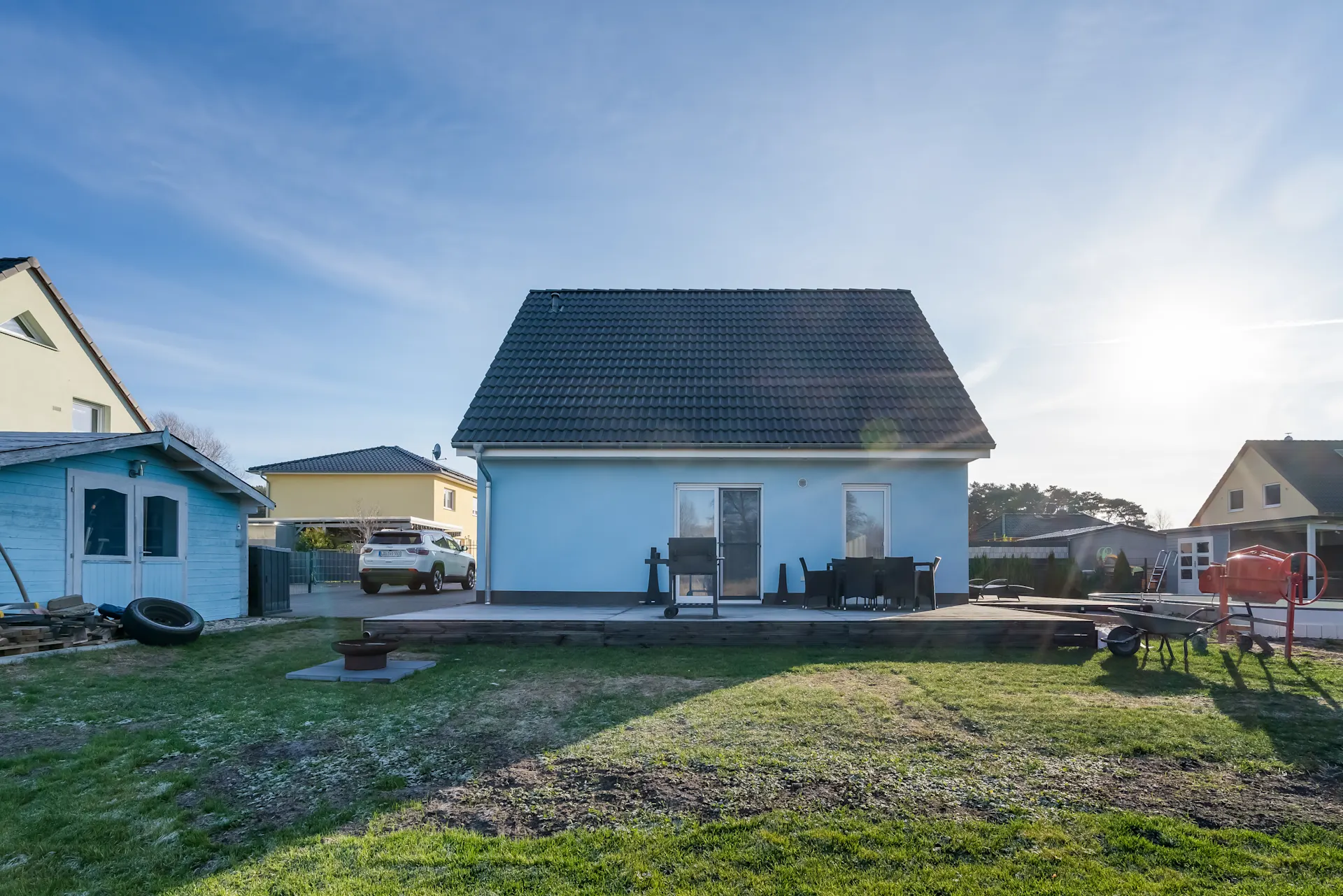 Blaues Einfamilienhaus mit Terrasse, Gartenmöbeln und Rasenfläche im Vordergrund.