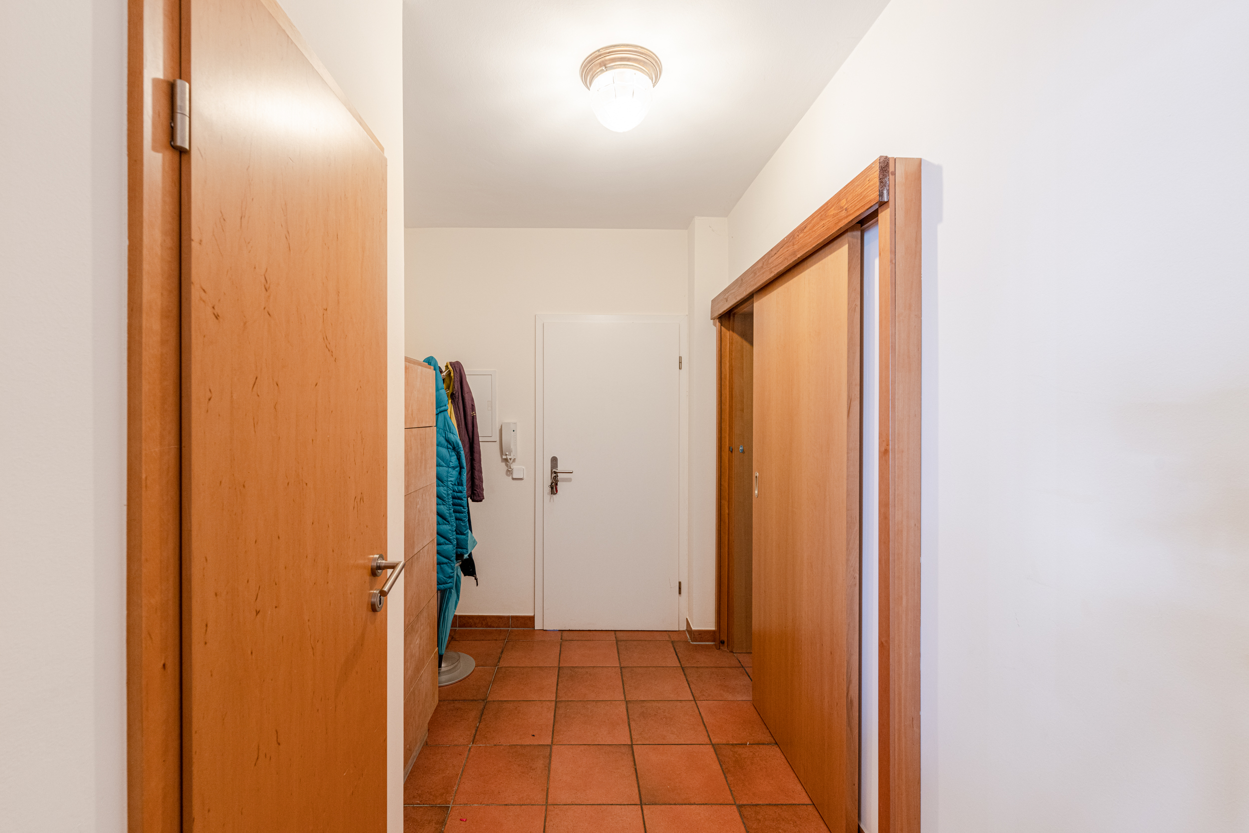 Flur mit Fliesenboden, Holztüren, Garderobe und Jacken an der Wand.