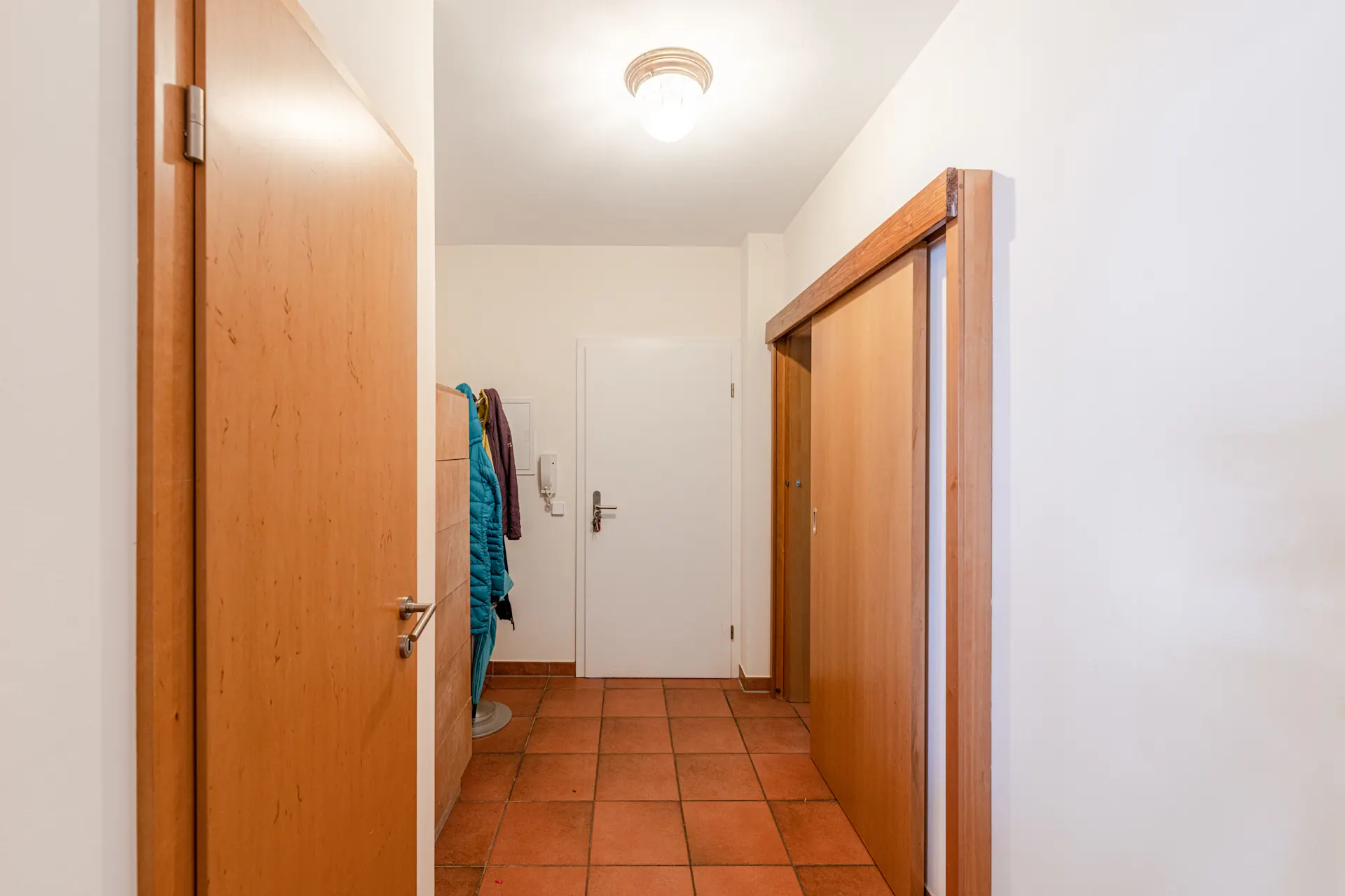 Flur mit Fliesenboden, Holztüren, Garderobe und Jacken an der Wand.