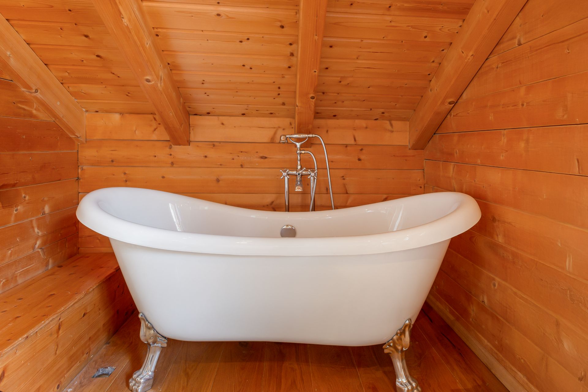 Freistehende weiße Badewanne in einem Badezimmer mit Holzverkleidung und Dachschräge.