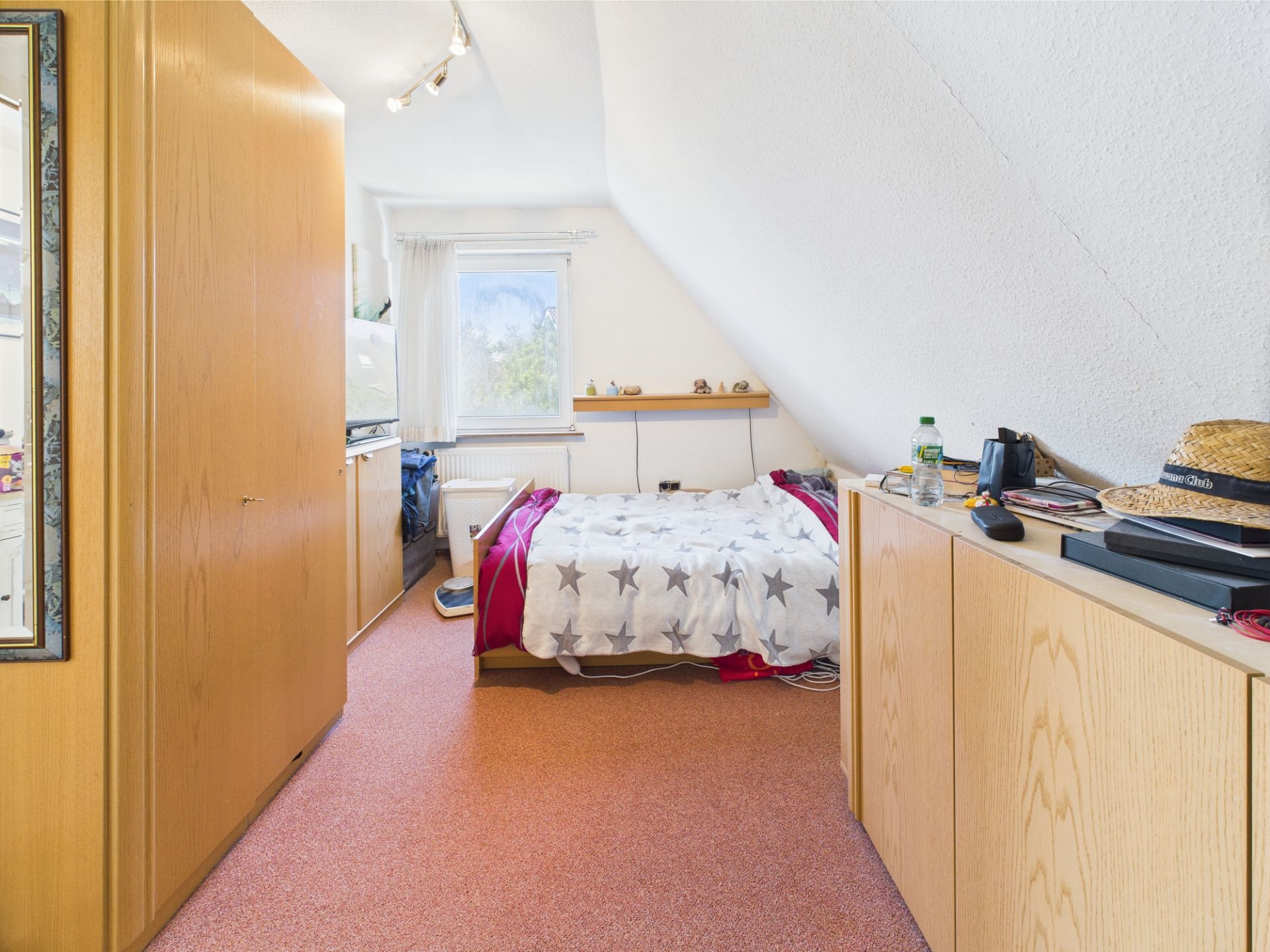 Schlafzimmer mit Einzelbett, Kommoden, Fenster und Dachschräge.