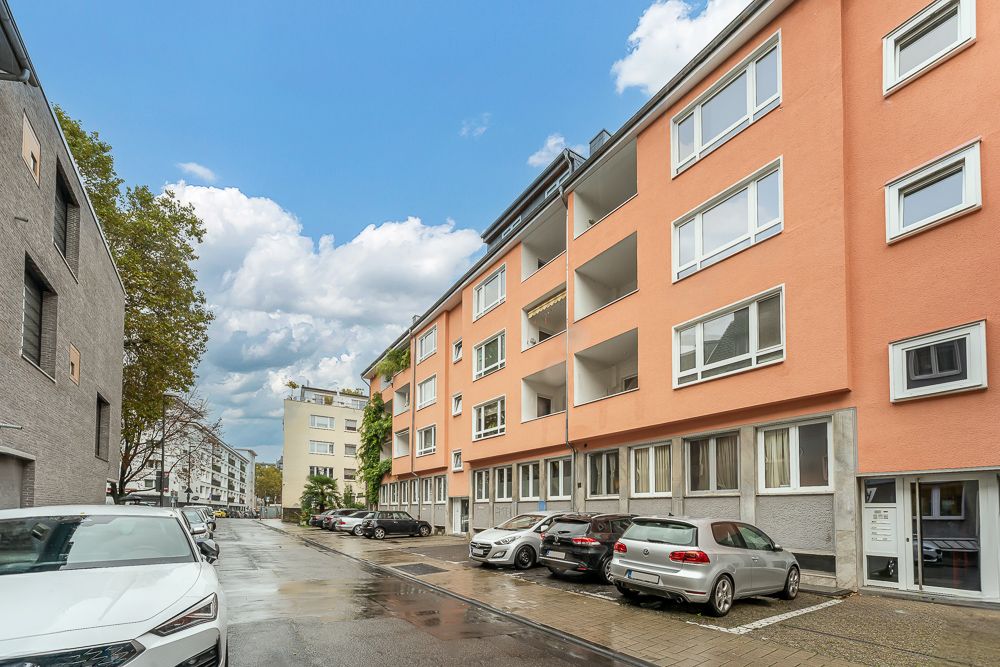 Wohngebäude mit orangefarbener Fassade, geparkte Autos davor, Straßenansicht bei Tageslicht.