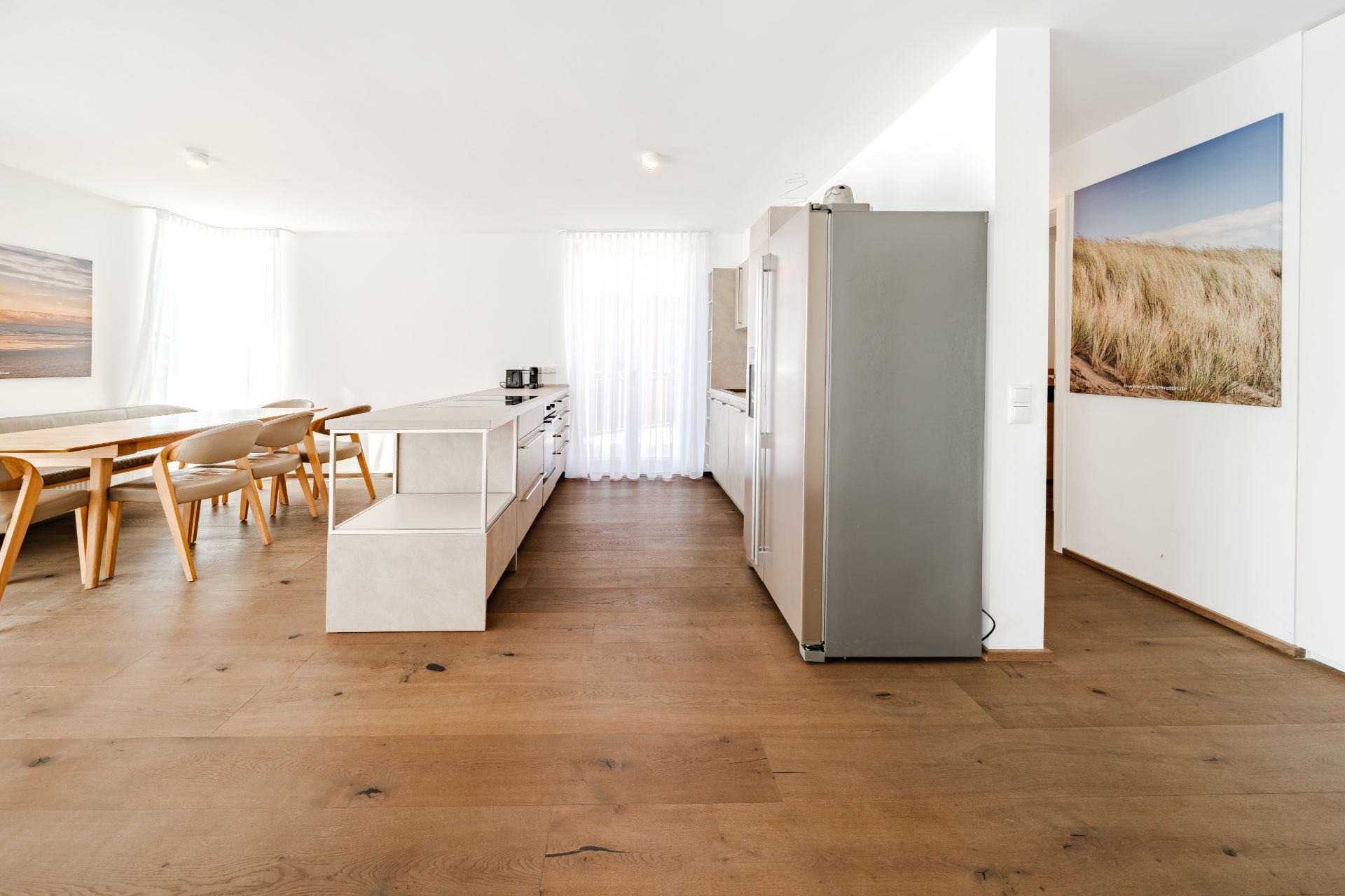 Helle, moderne Wohnküche mit Esstisch, Kücheninsel und großem Kühlschrank auf Holzfußboden.