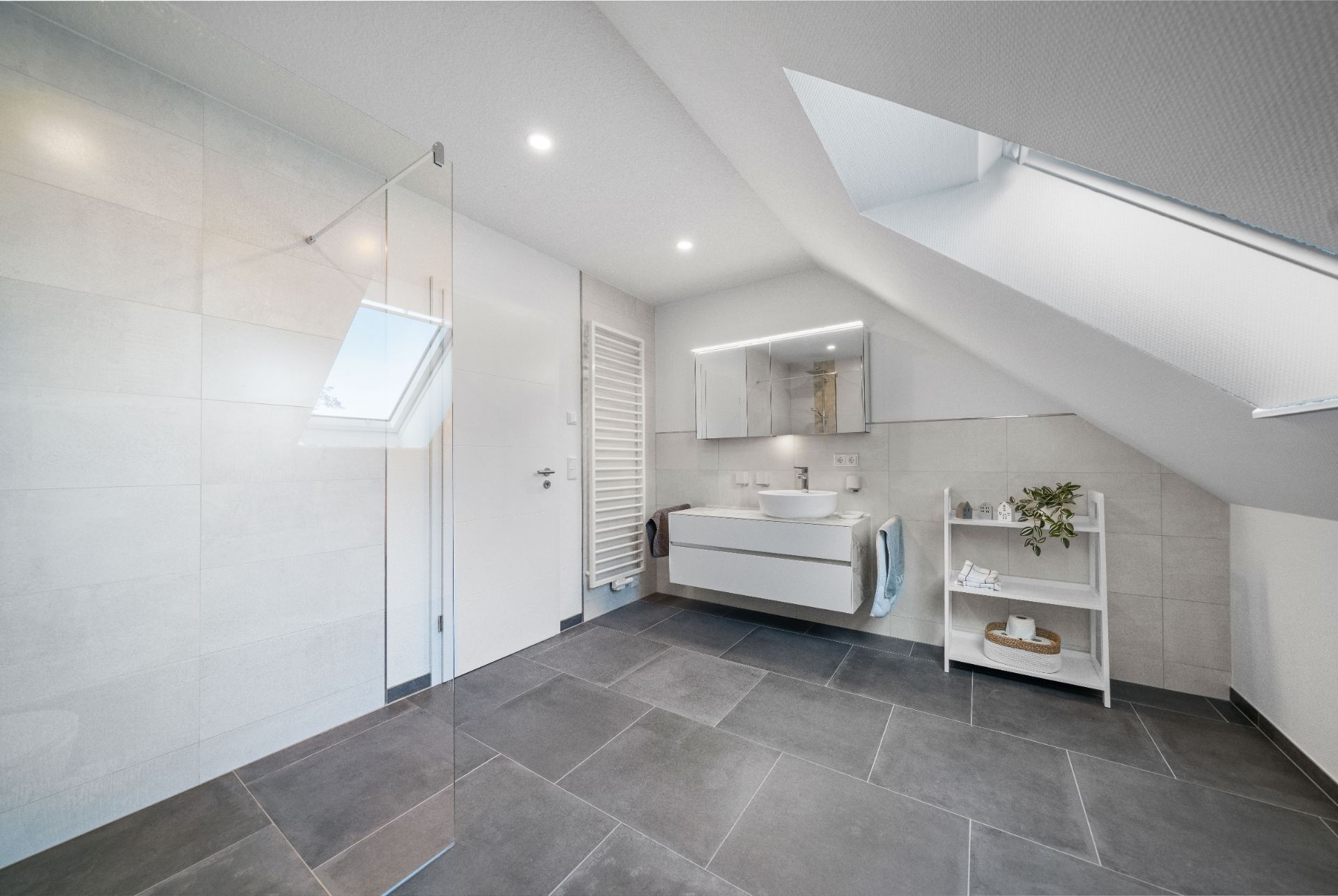 Modernes Bad mit Dachfenster, Waschbecken, Spiegel, Glasdusche und Regal auf dunklem Fliesenboden.