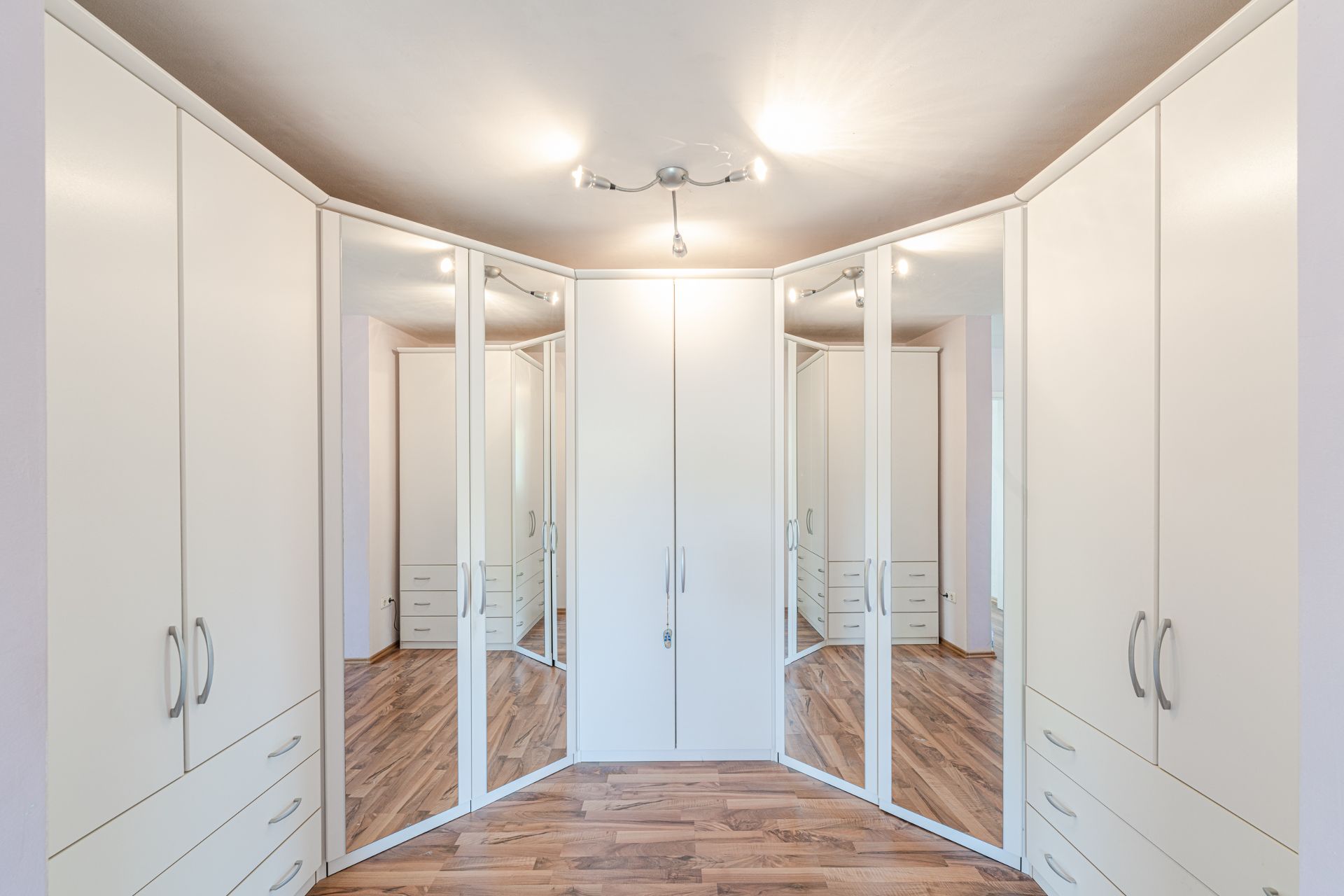 Großer Einbauschrank mit weißen Türen und Spiegeln in einem Raum mit Holzfußboden.