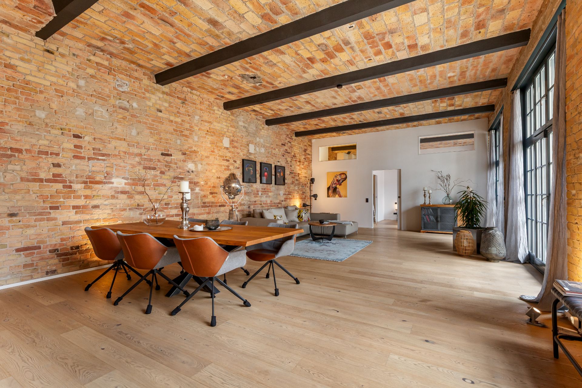 Heller Wohn- und Essbereich mit Backsteinwand, Holzboden, Tisch, Stühlen und Sofaecke.