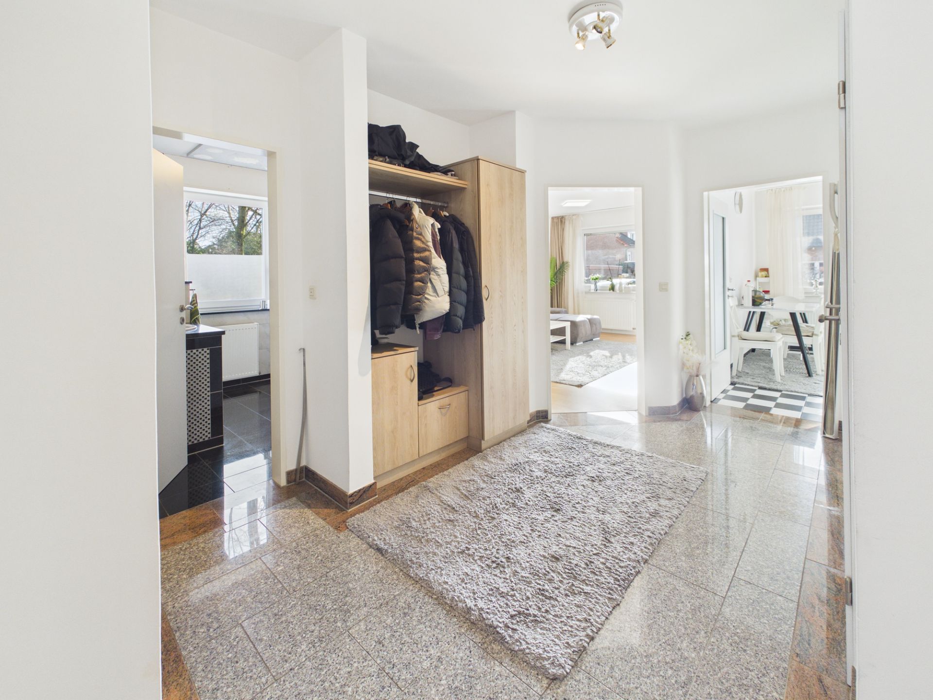 Heller Flur mit Kleiderschrank, Teppich und Blick in Wohnzimmer und weiteres Zimmer.