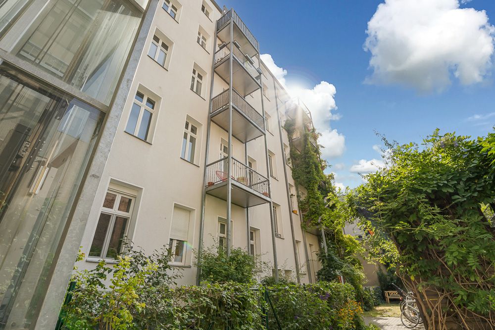 Innenhof eines Mehrfamilienhauses mit Balkonen, viel Grün und einem Glasaufzug links.