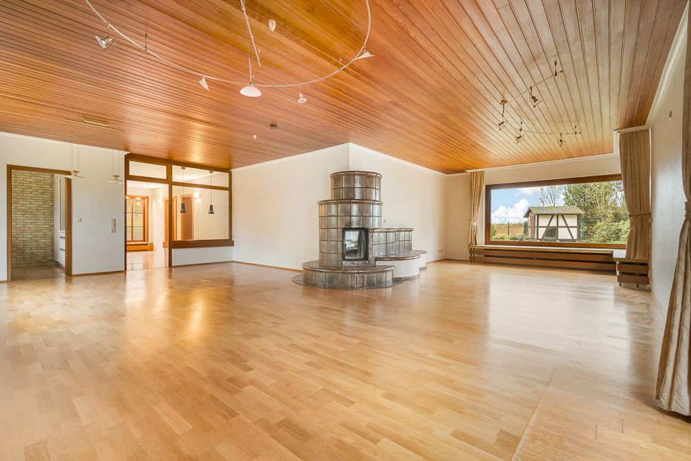 Großes, leeres Wohnzimmer mit Holzdecke, Kamin und großem Fenster mit Blick nach draußen.
