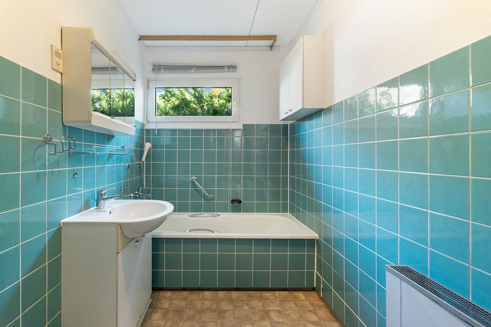Badezimmer mit grünen Fliesen, Badewanne, Waschbecken und Fenster.
