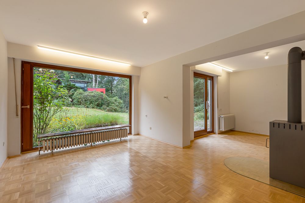 Helles Wohnzimmer mit Parkettboden, großen Fenstern und Blick ins Grüne.