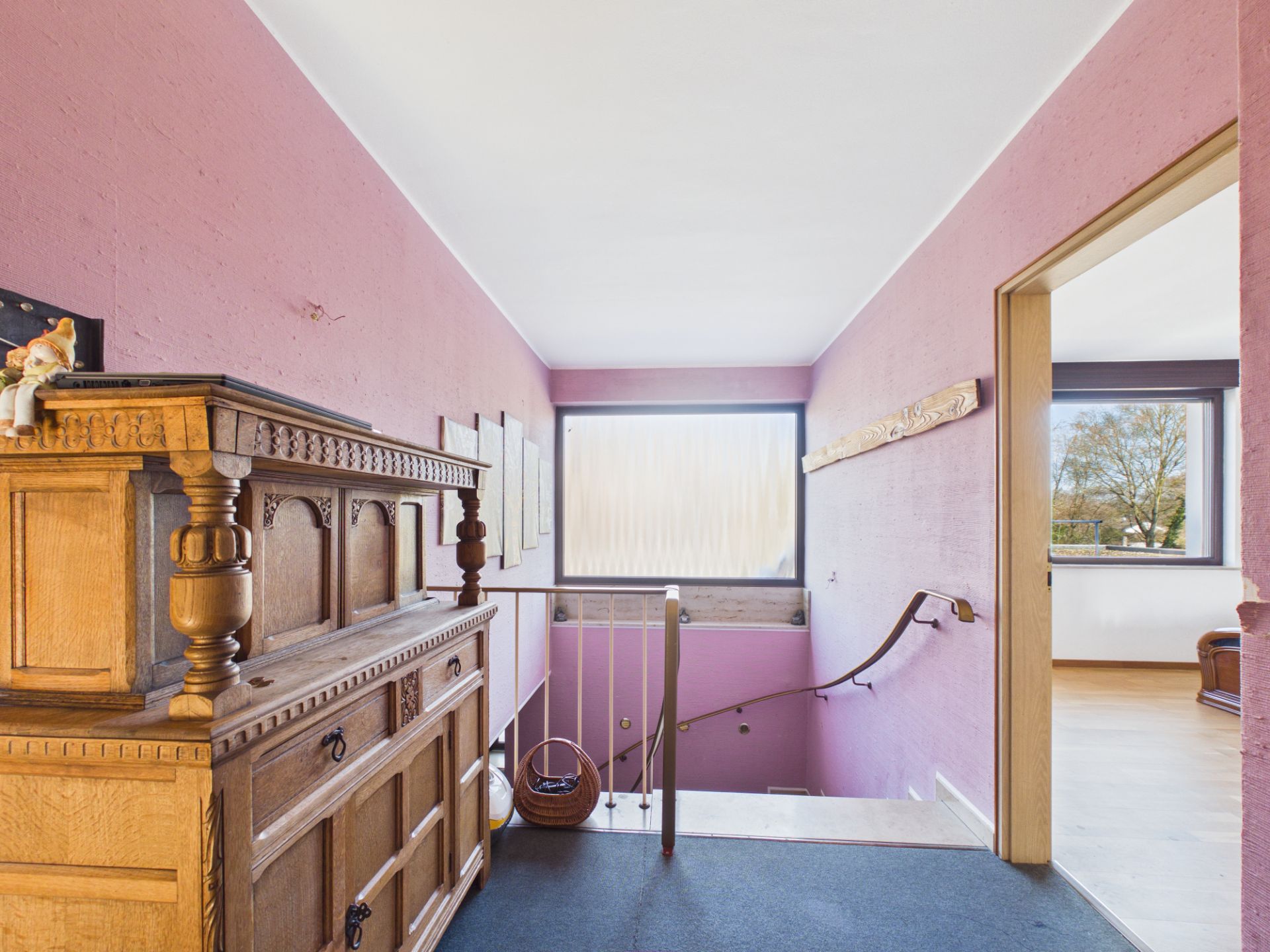 Flur mit rosa Wänden, altem Holzschrank und Treppe, großes Fenster im Hintergrund.