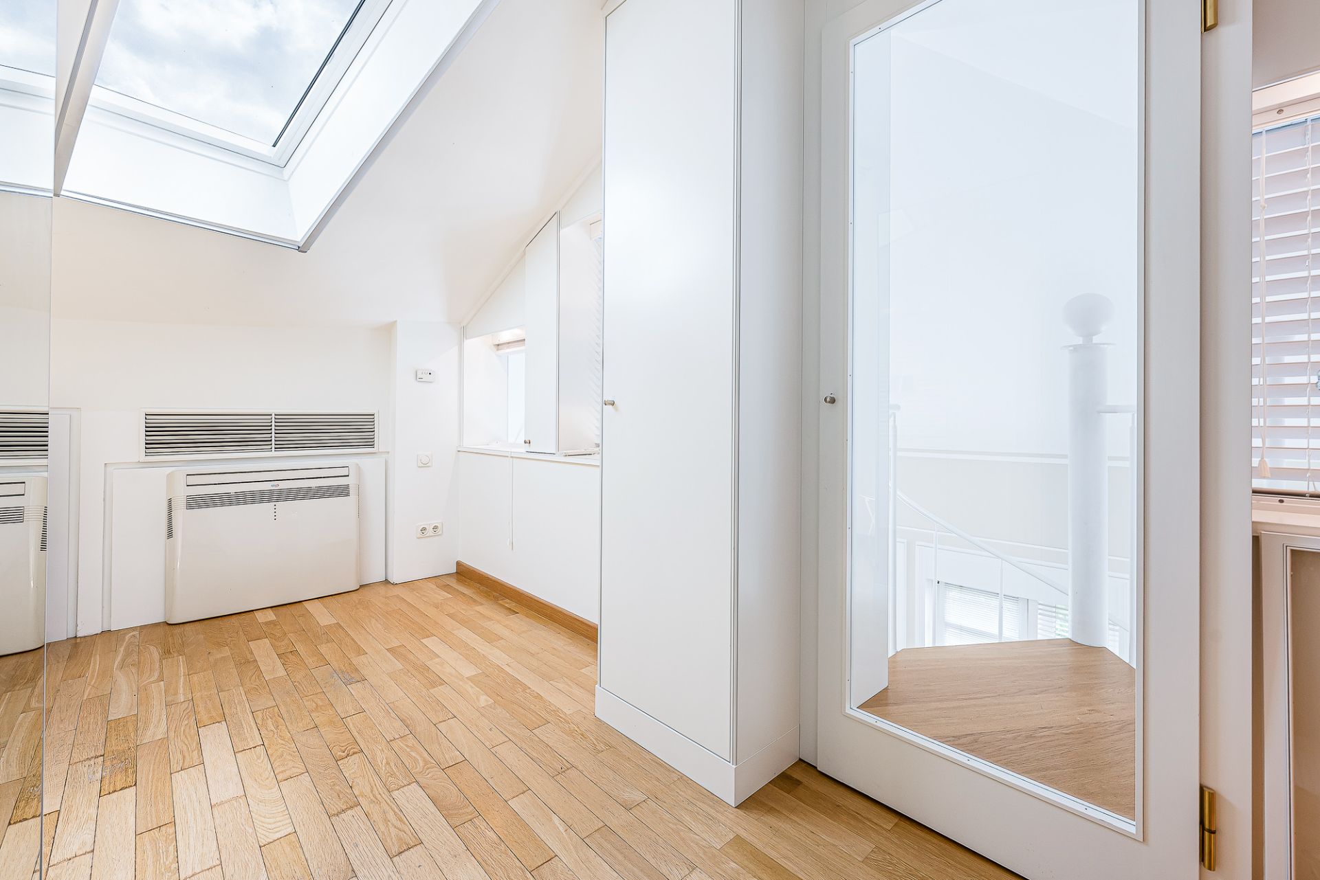 Heller Raum mit Dachfenster, Holzboden, weißen Wänden und Glastür.
