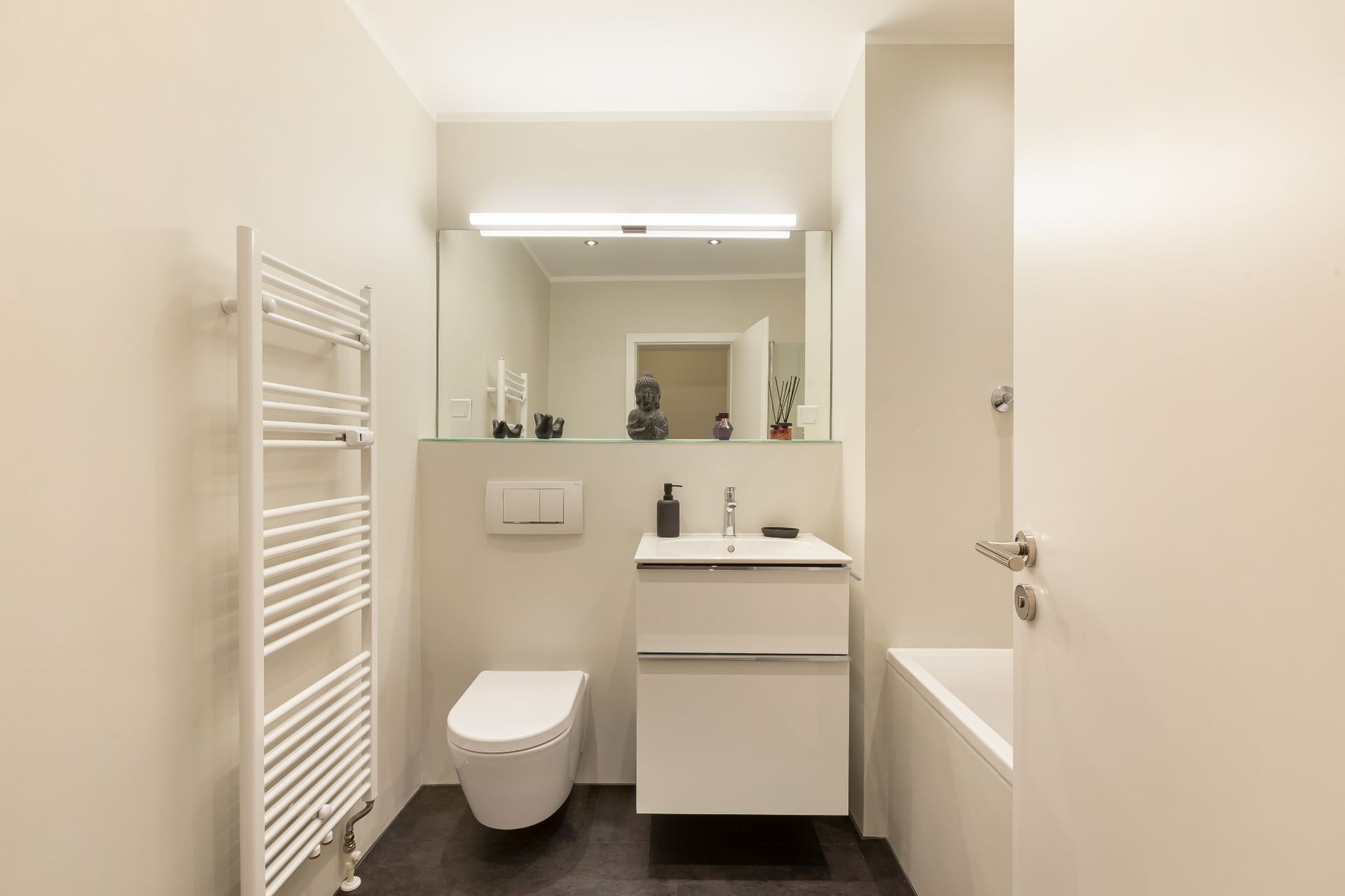 Modernes Badezimmer mit Waschbecken, Wandtoilette, Badewanne und Handtuchheizkörper.