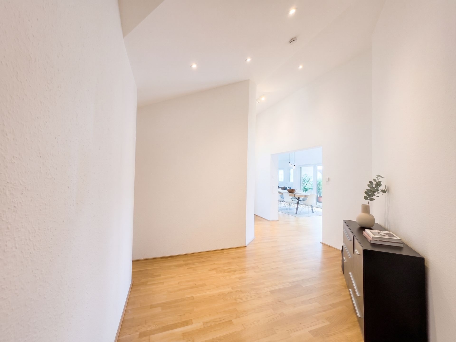 Heller Flur mit Parkettboden, Kommode an der rechten Wand, Blick ins Wohnzimmer.
