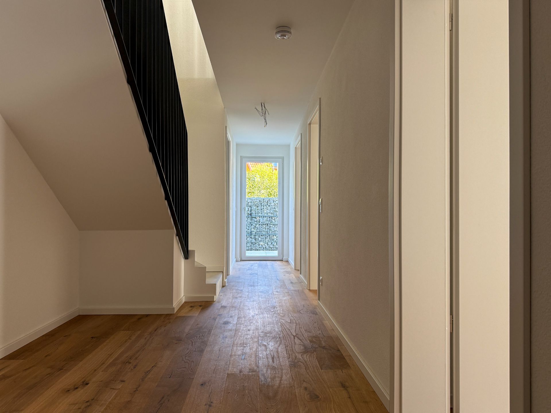 Heller Flur mit Holzfußboden und Treppe, Tür führt nach draußen.