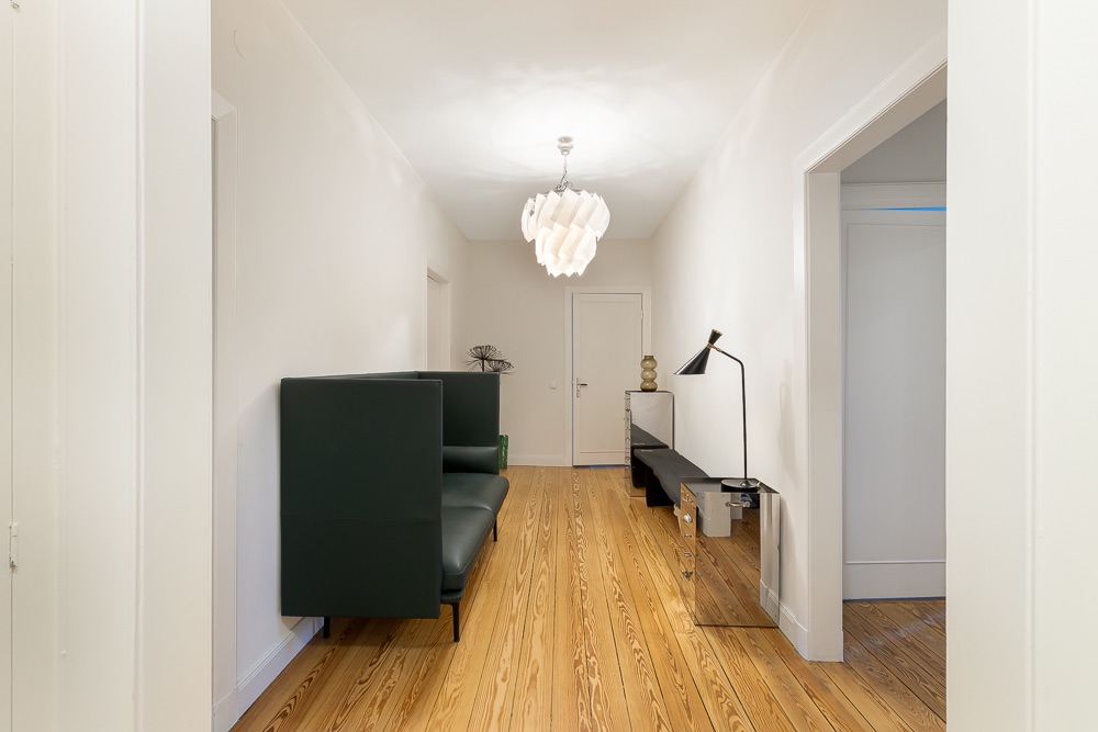 Heller Flur mit Holzboden, grüner Sitzbank, Sideboard und moderner Hängelampe.