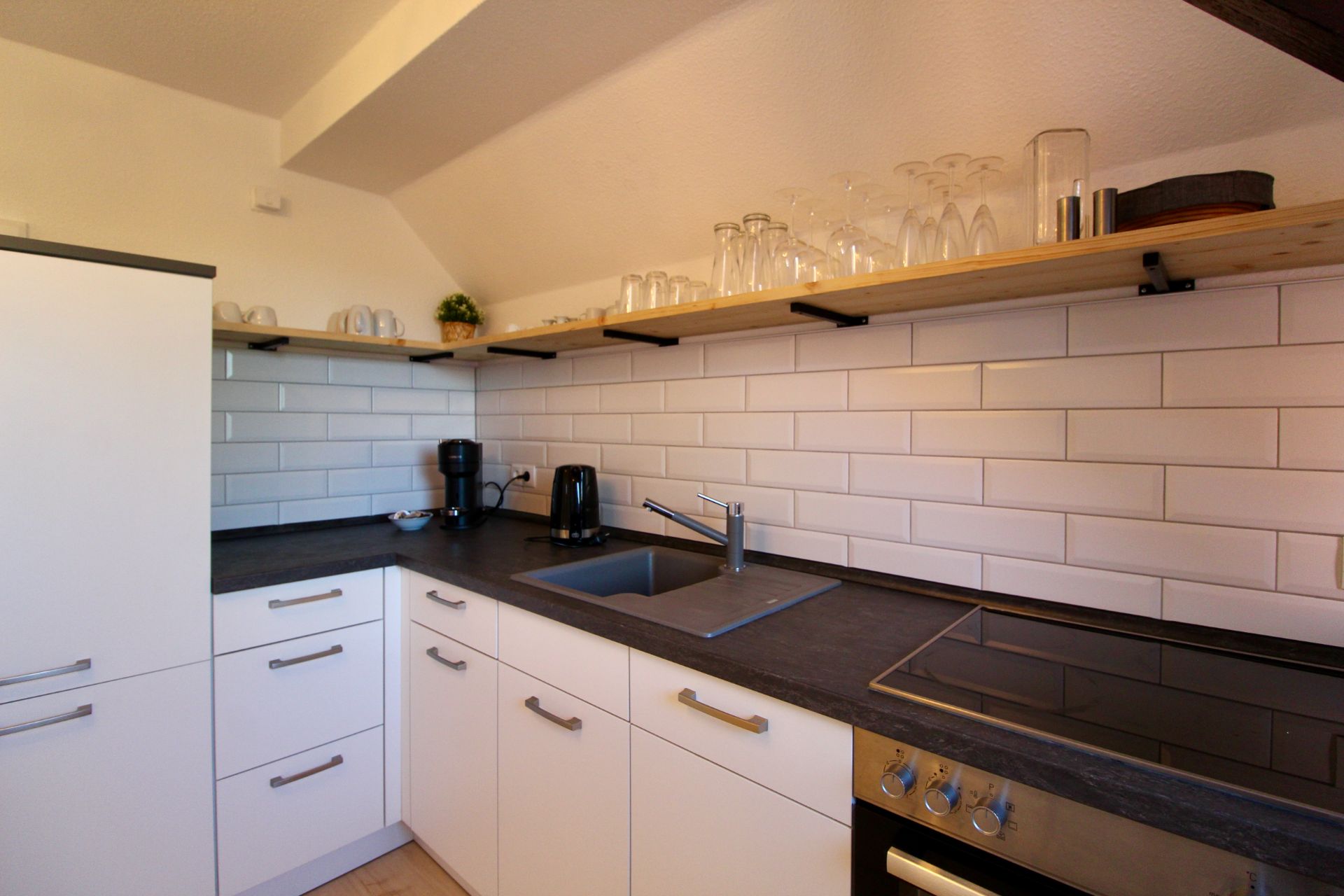 Moderne Küche mit weißen Schränken, Spüle, Herd und Regal mit Gläsern an der Wand.