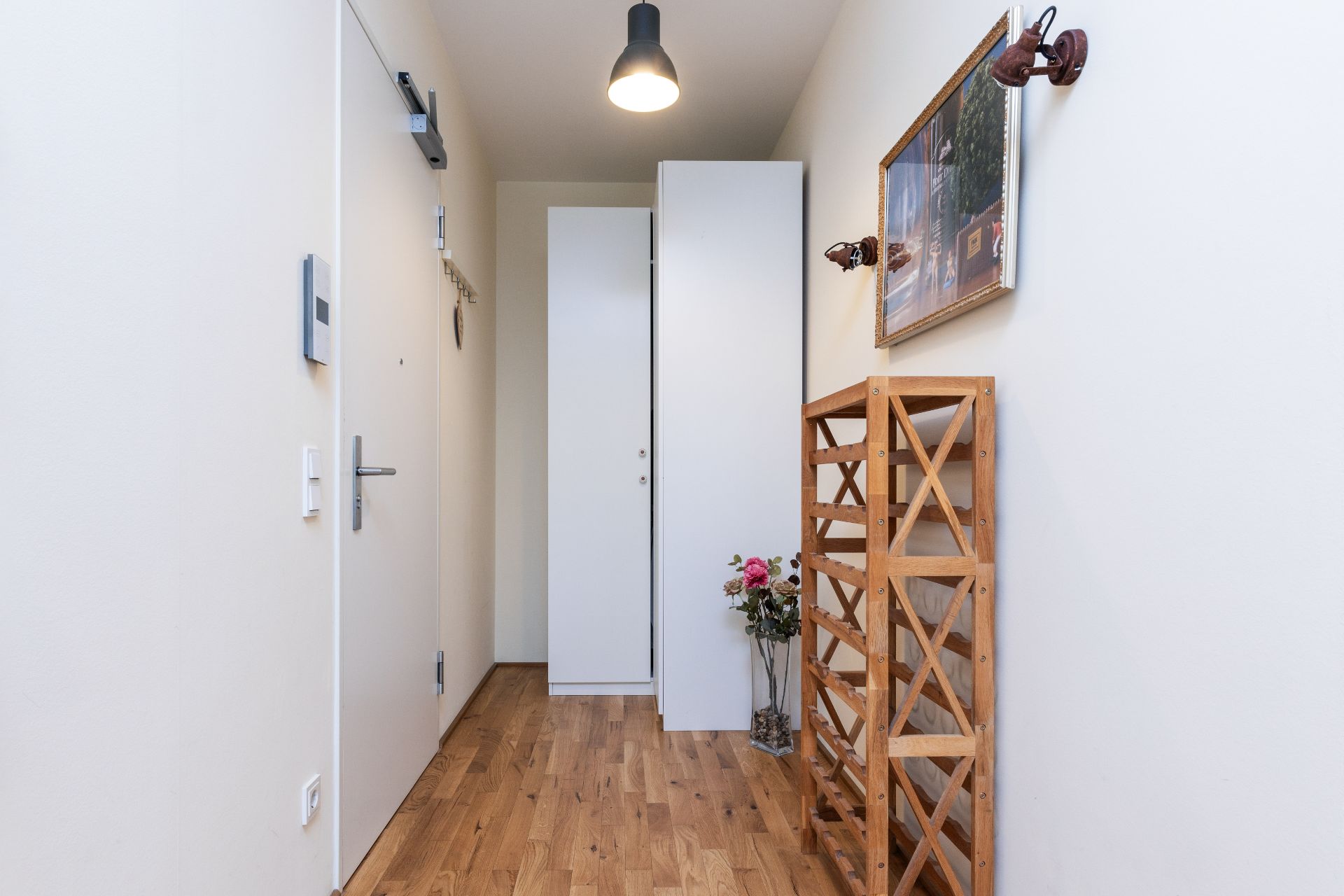 Heller Flur mit Holzfußboden, Garderobenschrank, Weinständer und einem Bild an der Wand.