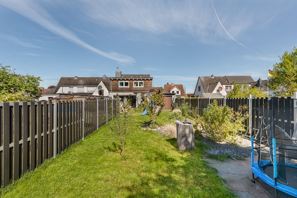 Langer Garten mit Rasenfläche, Bäumen, einem Zaun und einem blauen Trampolin rechts.