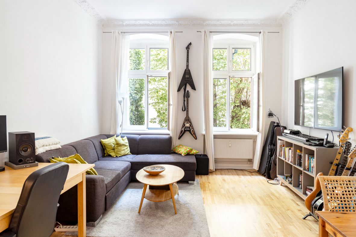Helles Wohnzimmer mit Sofa, Couchtisch, Gitarren, Regal und großem Fenster.