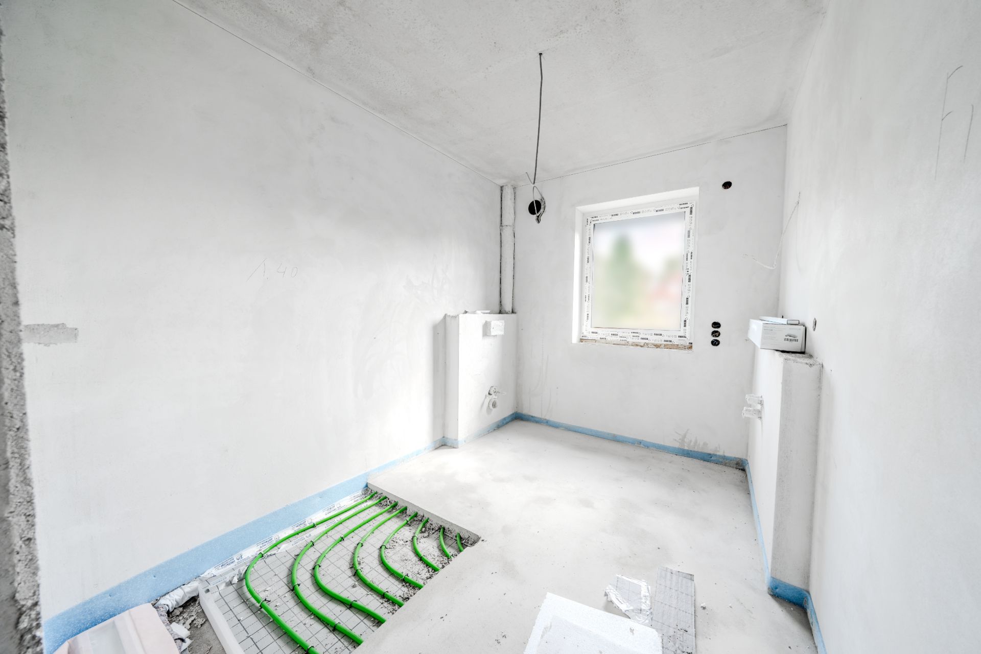 Heller Raum im Rohbau mit leerem Fenster und sichtbarer Fußbodenheizung.