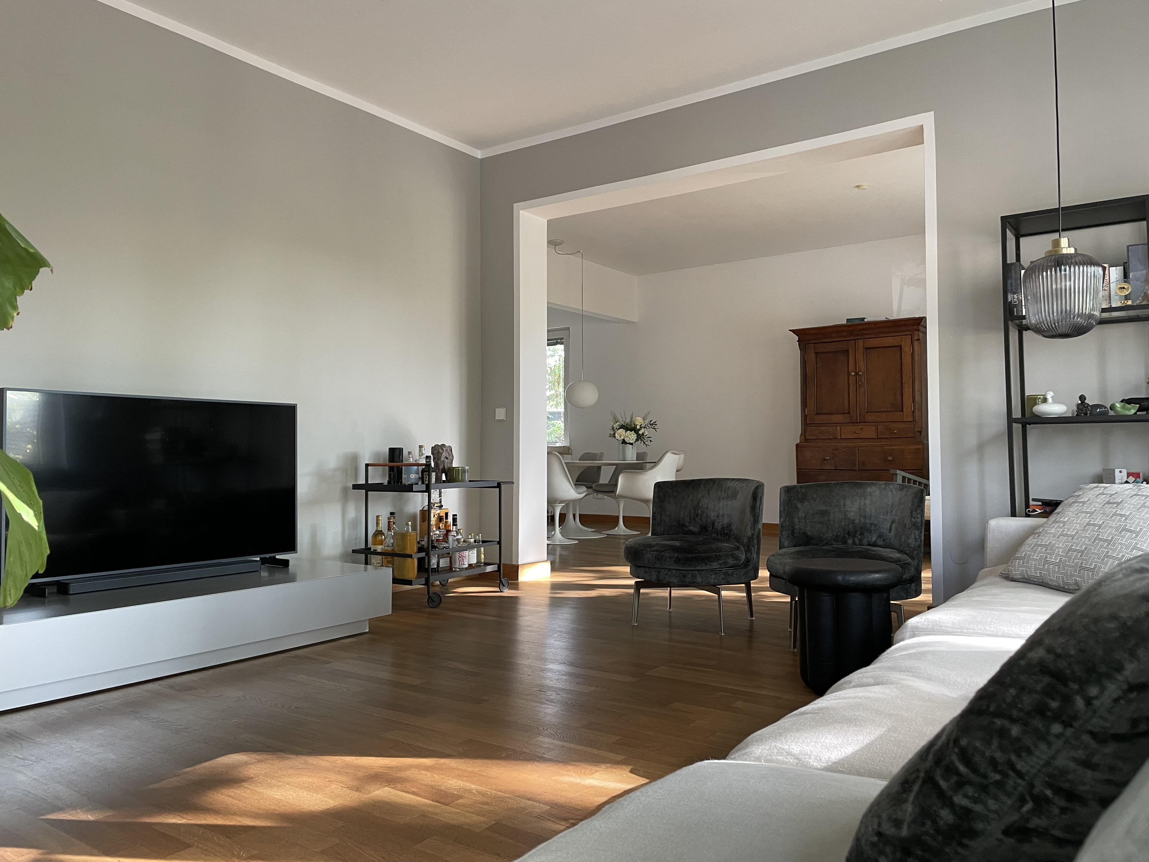 Modernes Wohnzimmer mit Fernseher, Sofa, Sesseln, Regal und Blick auf Essbereich mit Holzmöbel.