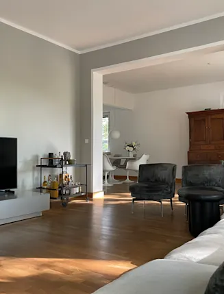 Modernes Wohnzimmer mit Fernseher, Sofa, Sesseln, Regal und Blick auf Essbereich mit Holzmöbel.