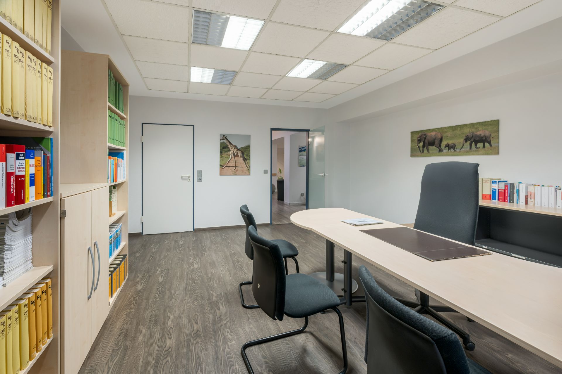 Helles Büro mit Schreibtisch, Stühlen und Bücherregalen voller Akten und Bücher.