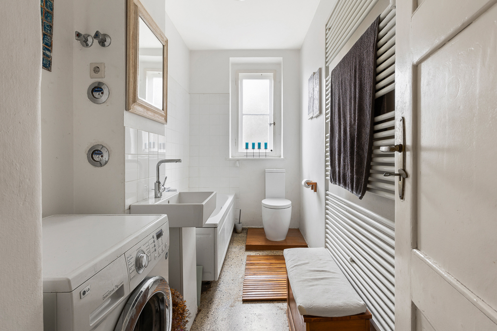 Helles Badezimmer mit Waschmaschine, Badewanne, Waschbecken, Toilette und Fenster.