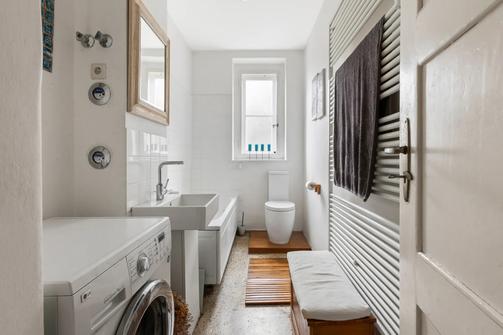 Helles Badezimmer mit Waschmaschine, Badewanne, Waschbecken, Toilette und Fenster.