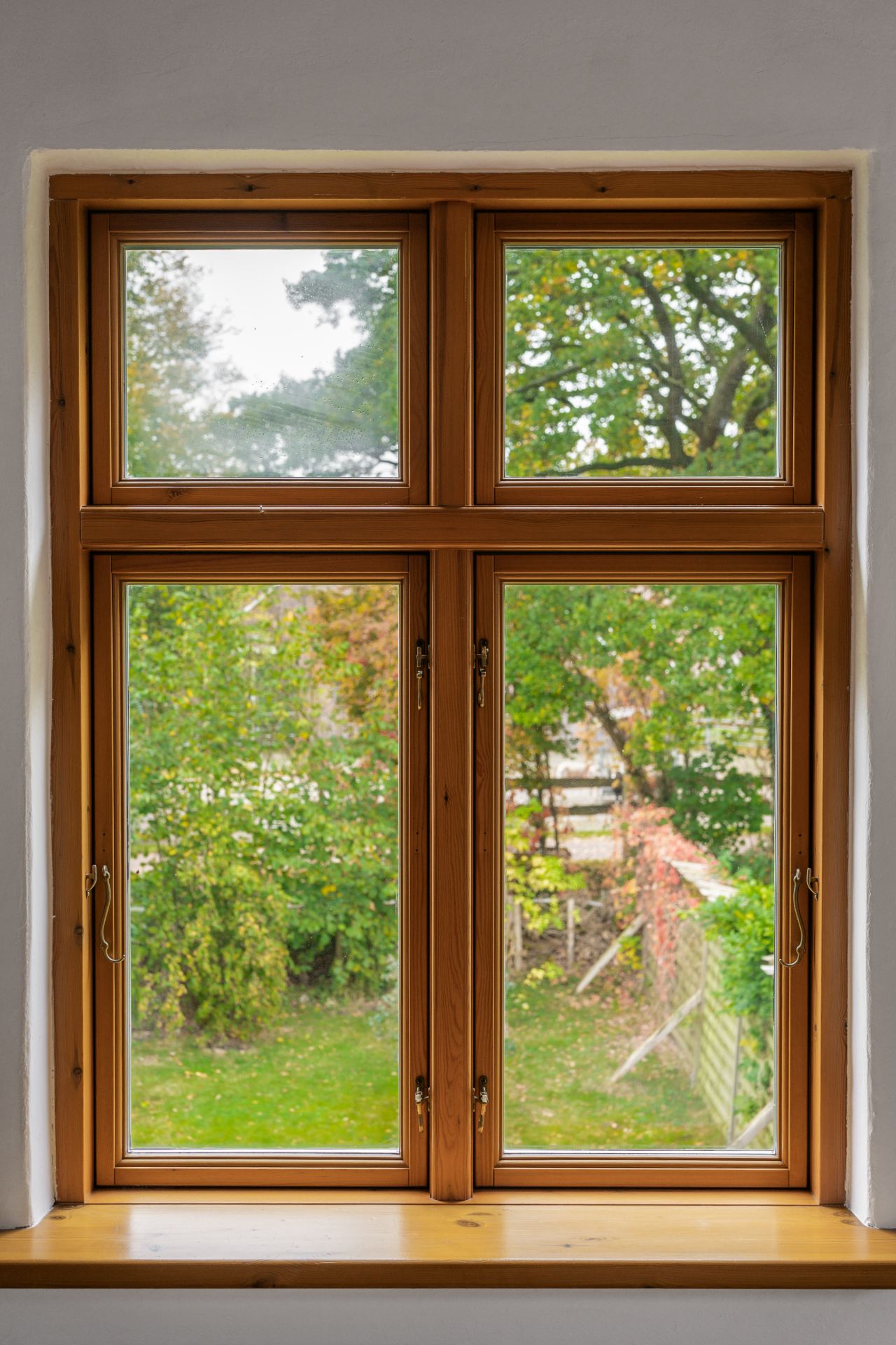 Holzrahmenfenster mit Blick auf einen Garten mit Bäumen und Sträuchern.